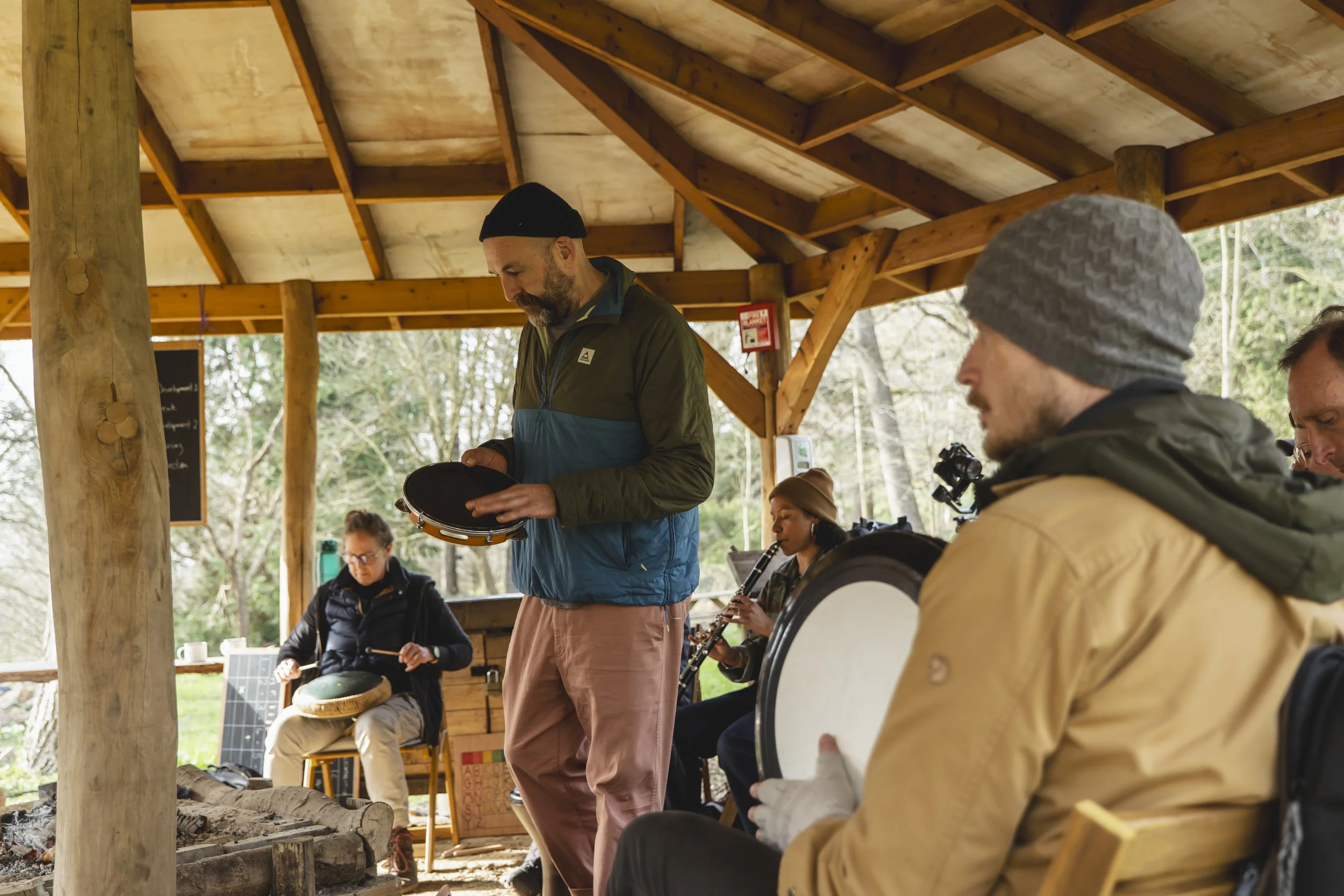 Group of people playing musical instruments together in a rustic outdoor shelter.