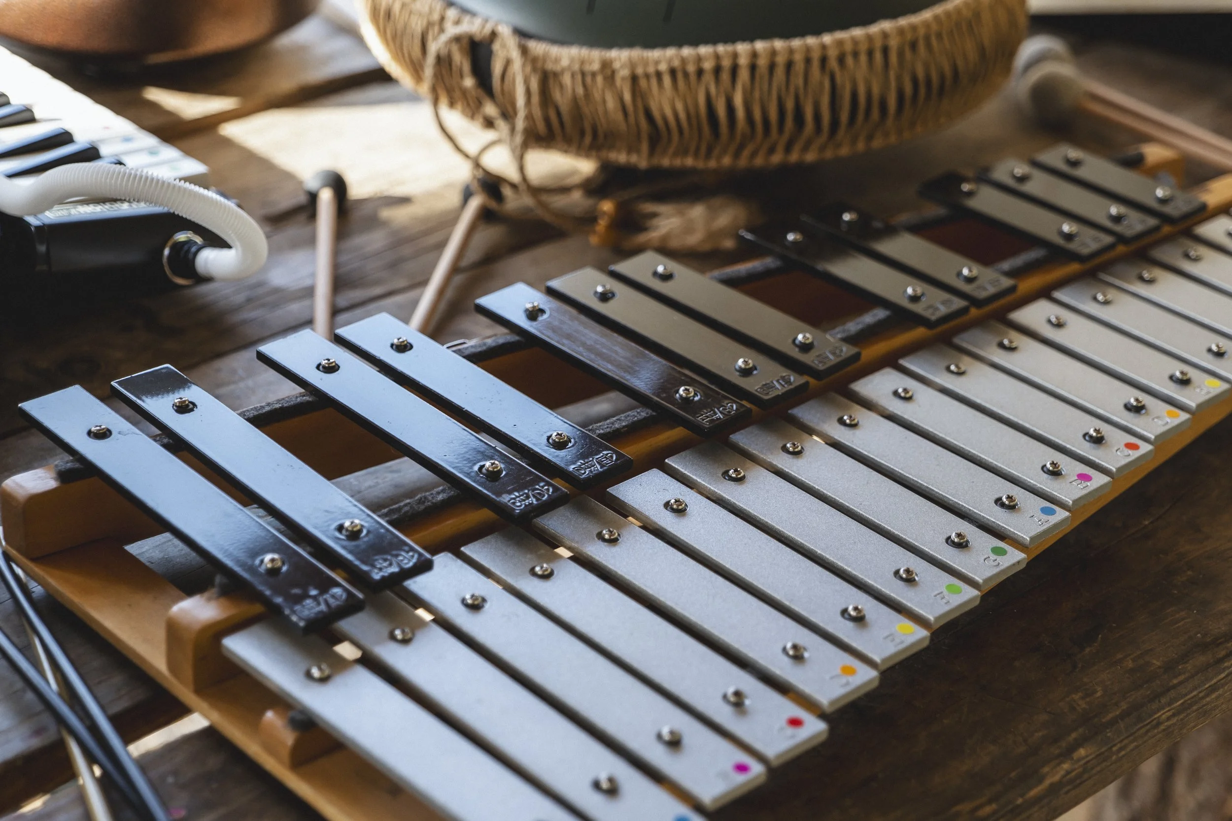 A xylophone with black and silver metal bars on a wooden table, with a basket nearby.