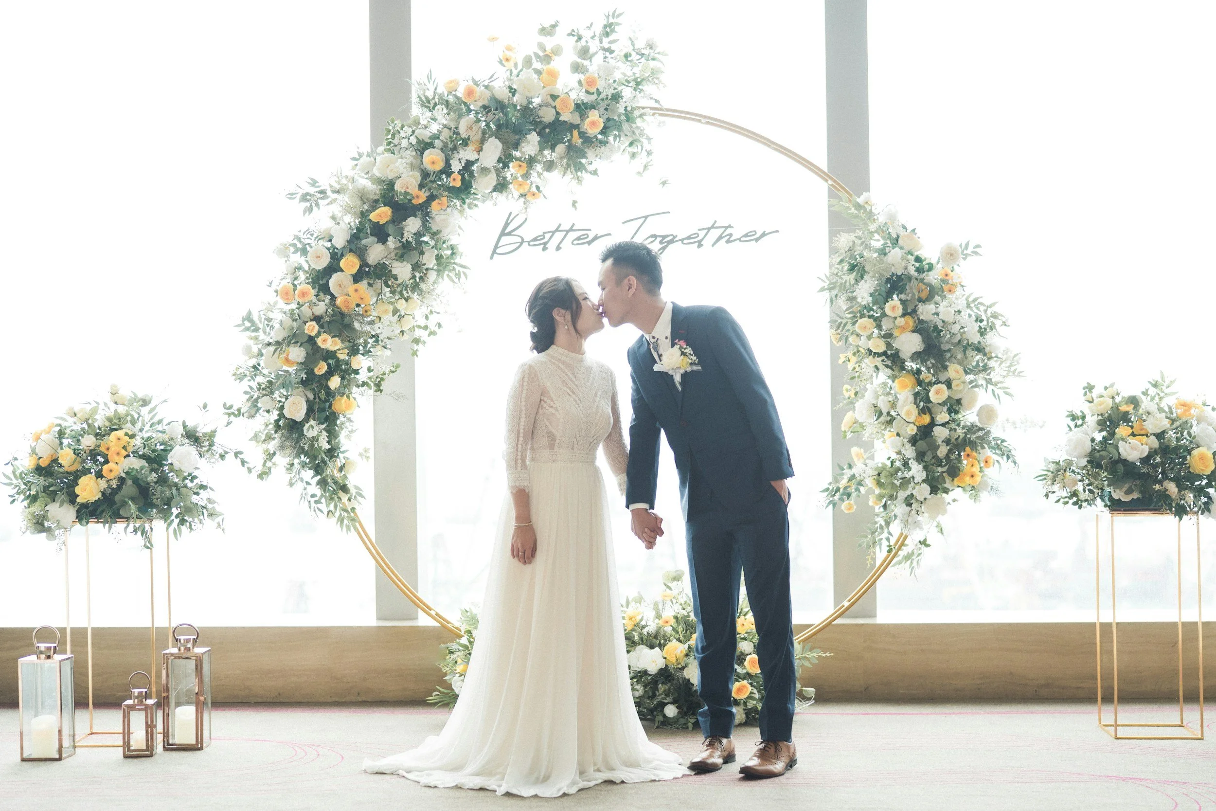Wedding couple kissing in front of floral hoop with custom sign, rentals by Honeyroom Event Rentals LLC in Branson, Mo.