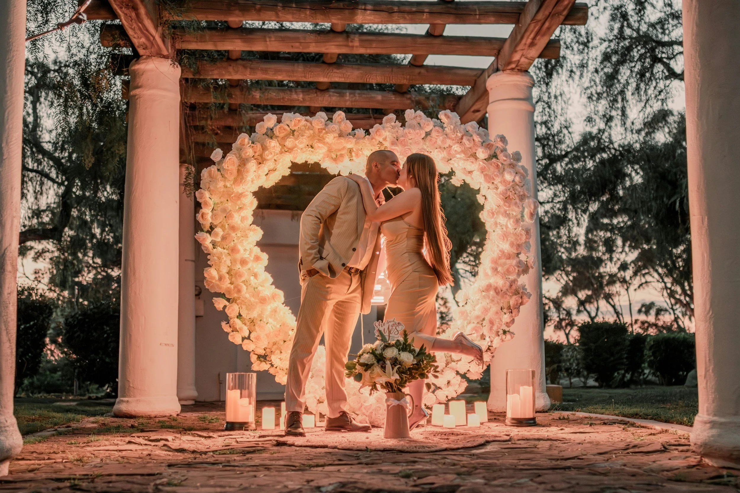 Couple kissing under a heart-shaped floral arch by Honeyroom Event  Rentals LLC.