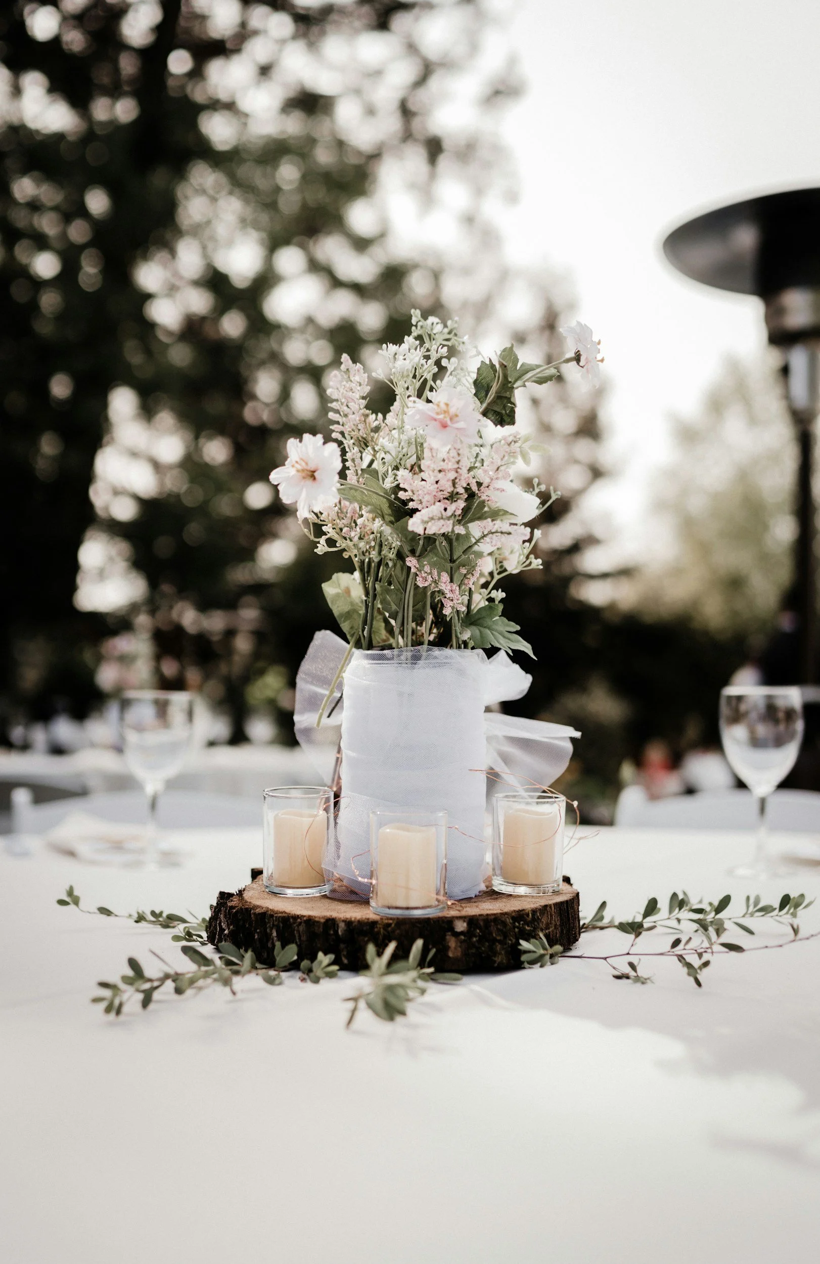 Beautiful wedding table centerpiece setup with candles, vases, floral, and garland for an outdoor wedding with rentals by Honeyroom Event Rentals LLC located in Branson, MO.