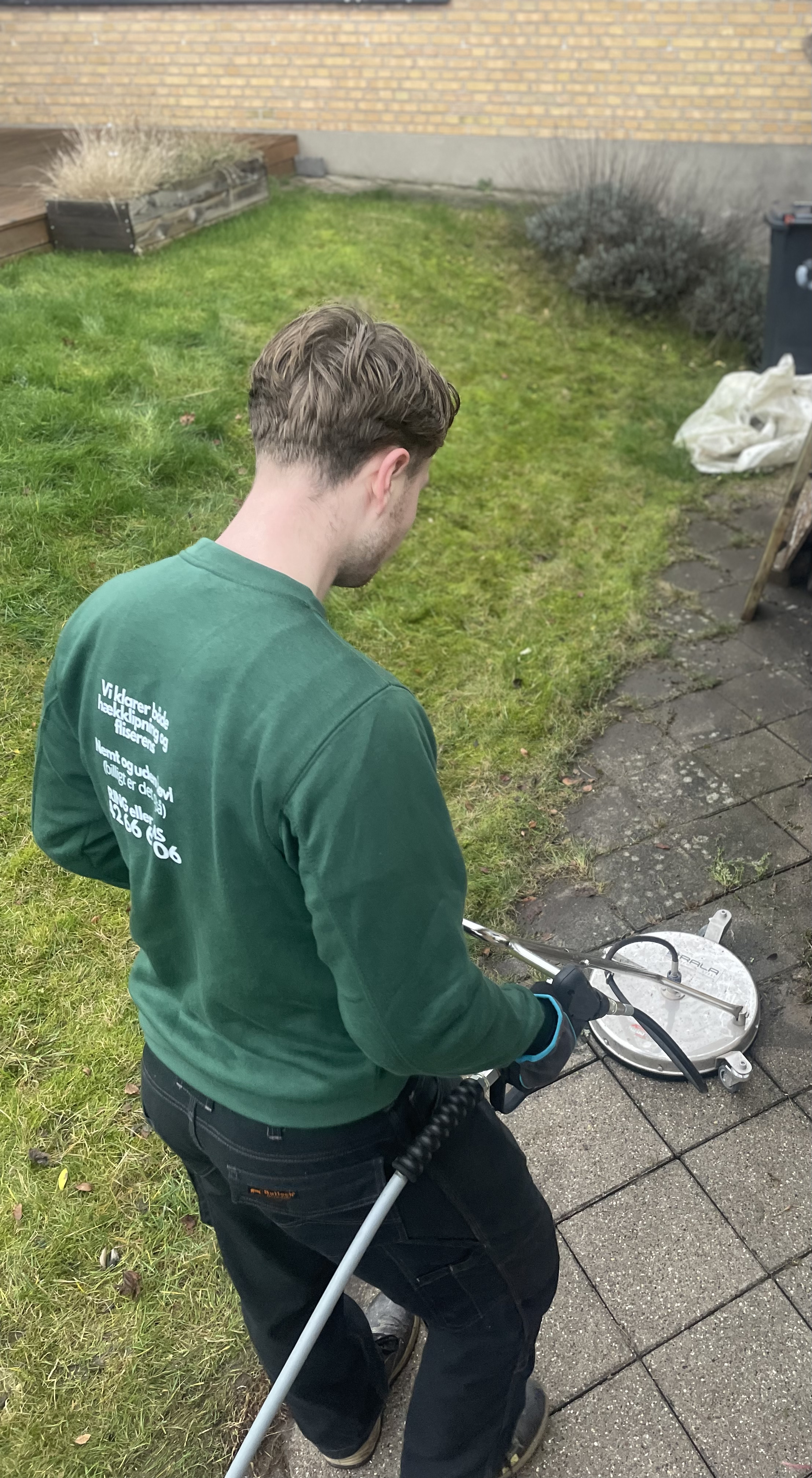 A man using a water pressure cleaner on a stone patio.