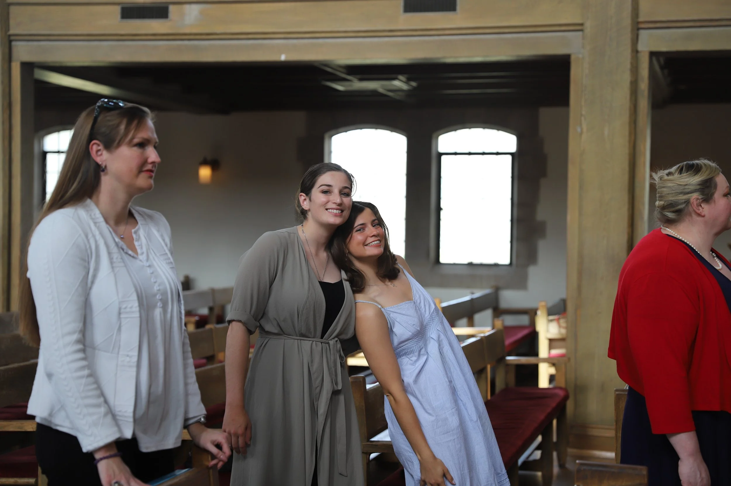 Four women standing in a church, smiling and posing for a photo, with benches and windows in the background.