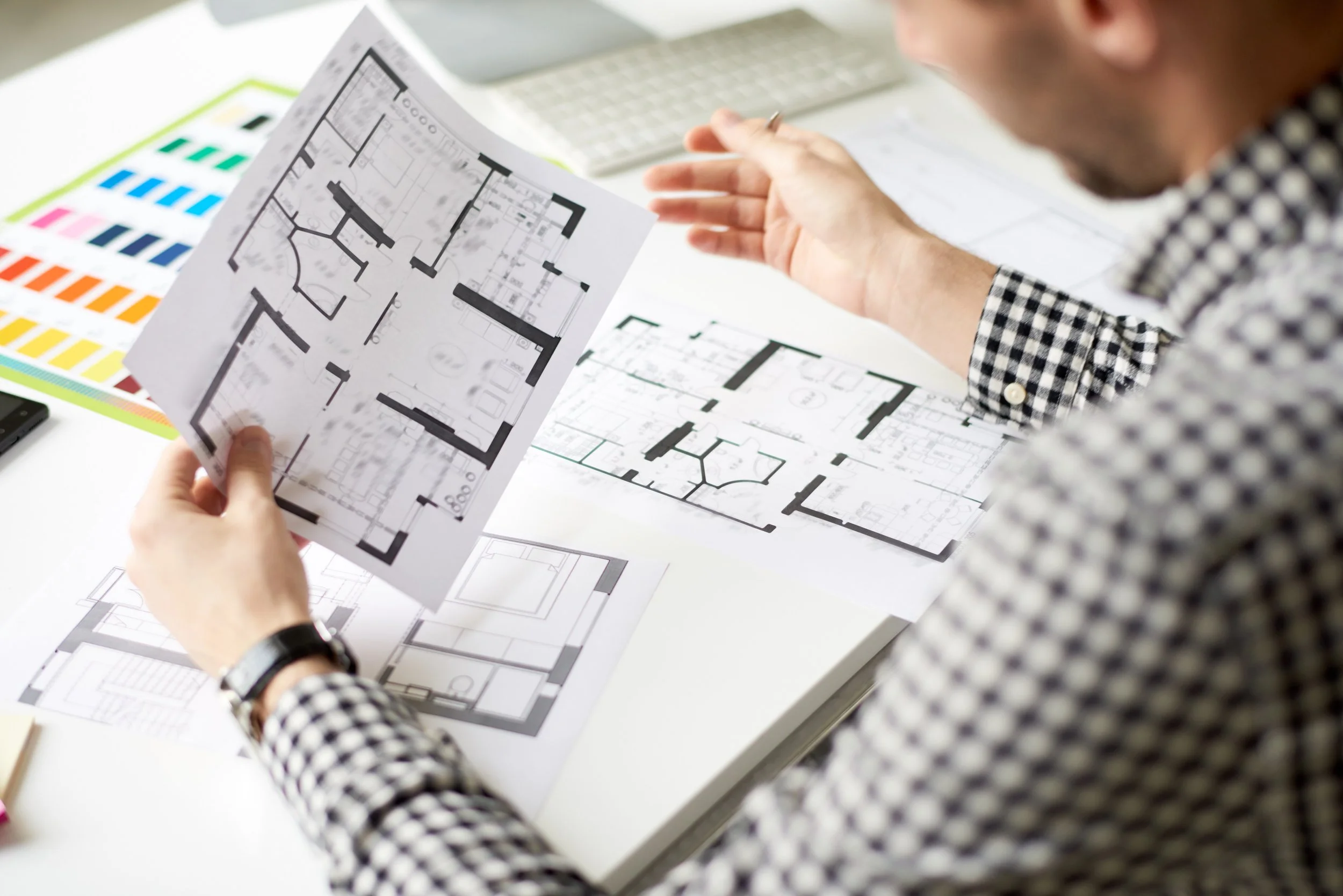 Person holding architectural floor plans and working on blueprints at a desk.