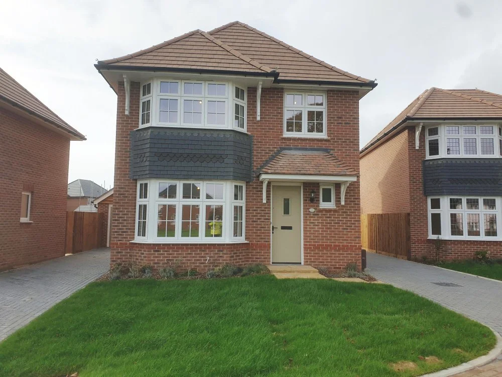 Front view of a two-story brick house with bay windows, a small porch, and a green lawn.