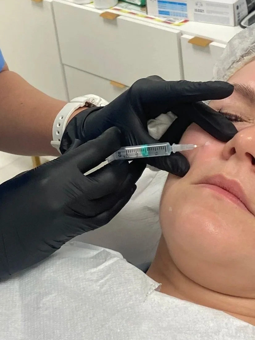 A medical professional administers an injection to a woman's nose in a clinical setting.