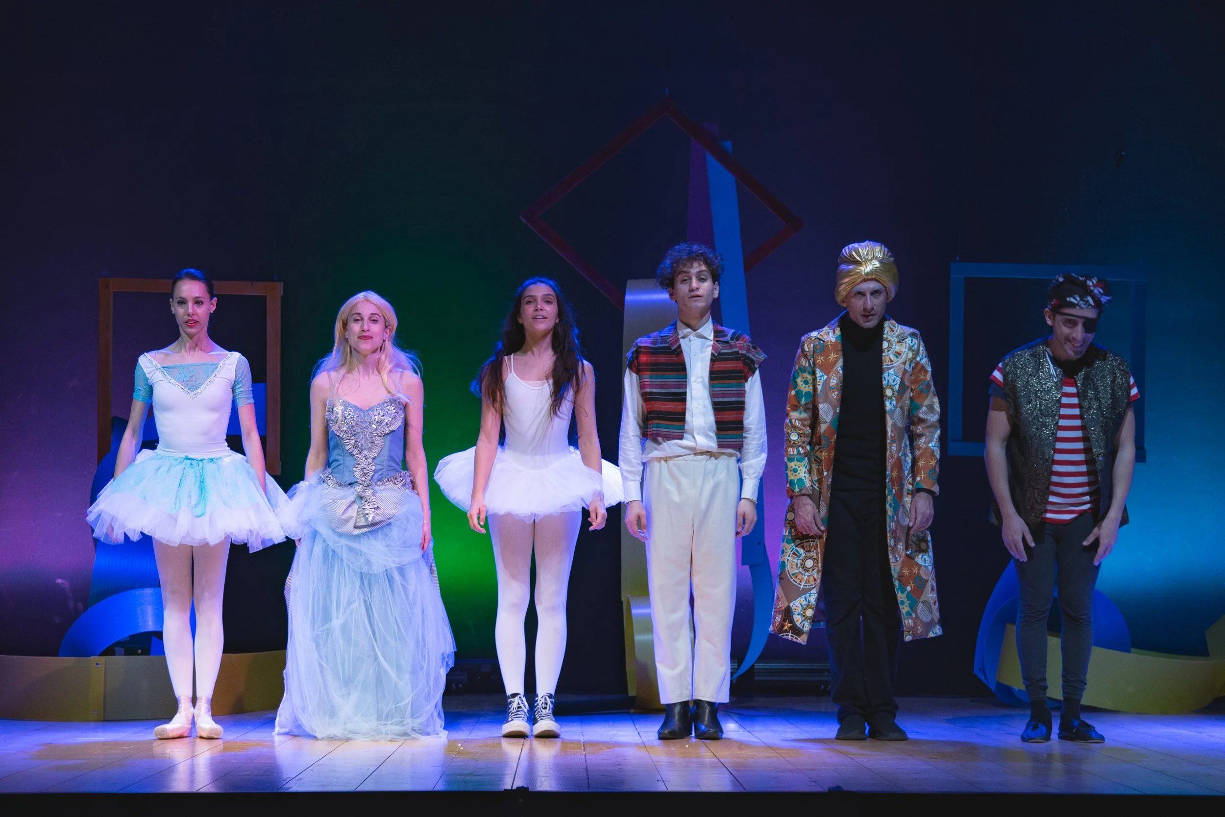 Un gruppo di sei attori sul palco dopo uno spettacolo teatrale, con abiti variopinti e sorrisi, in posa per una foto di gruppo.