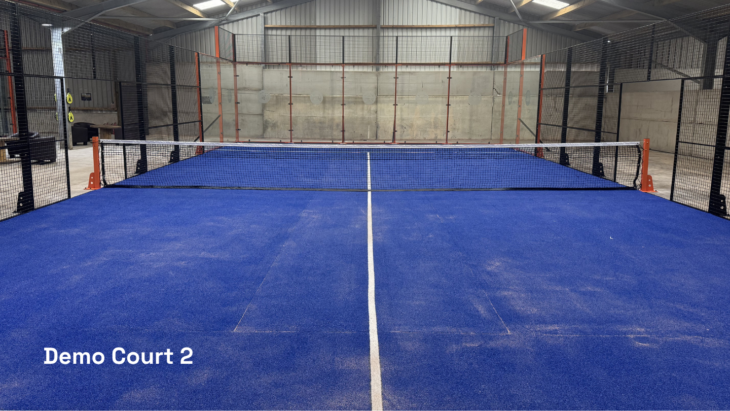 Indoor pickleball court with blue flooring, black mesh fencing, and orange support posts, labeled "Demo Court 2" in the lower left corner.