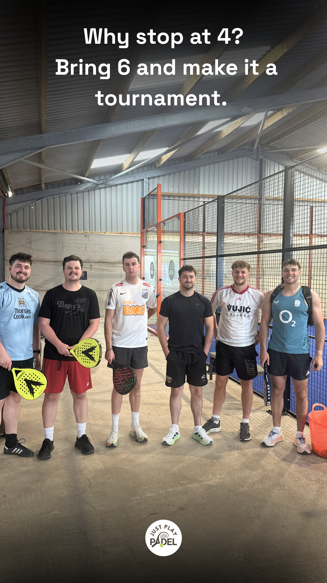 Group of six young men standing inside a padel court, holding paddles, smiling, with a metal fence and court wall in the background.