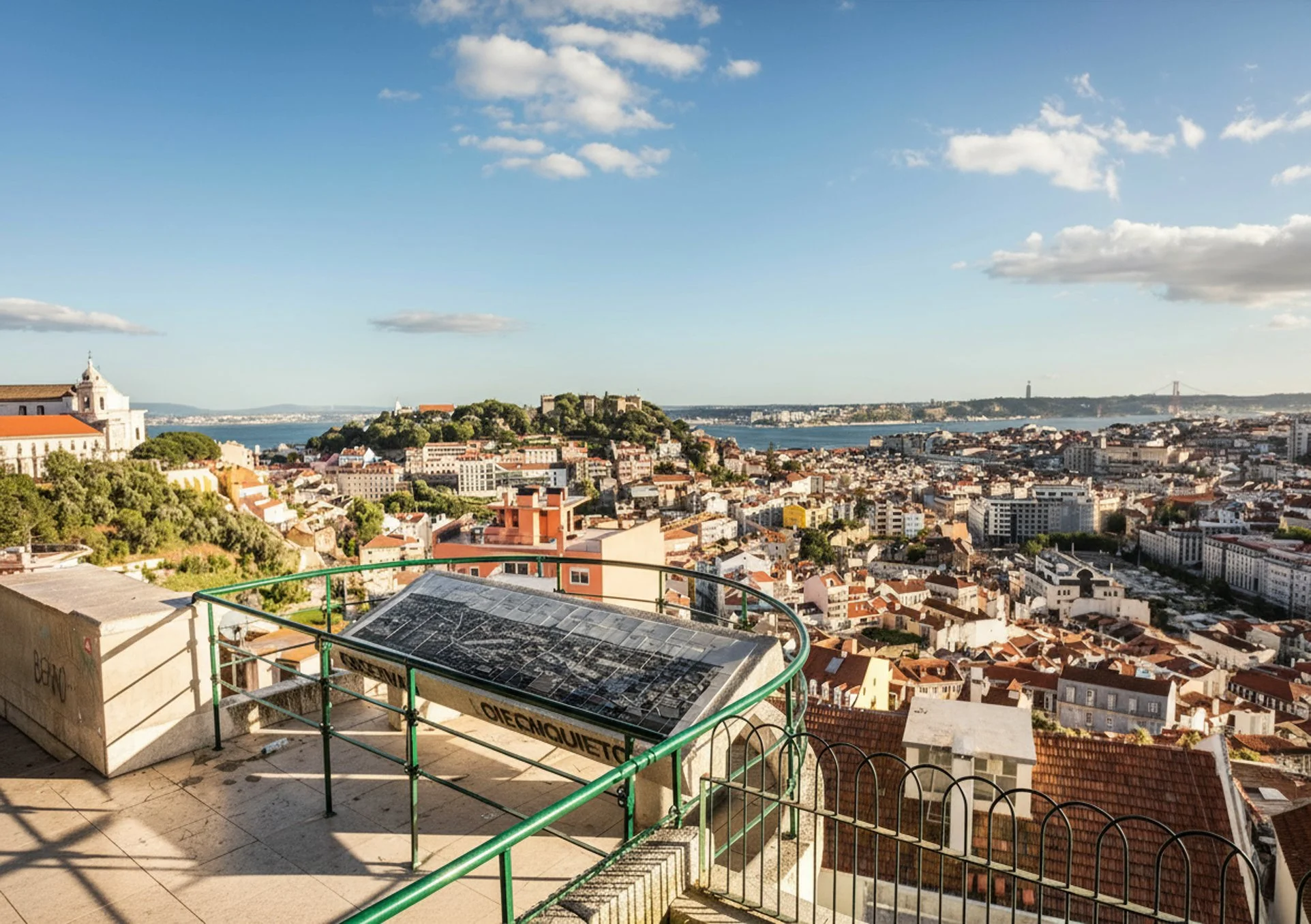 Vista de uma cidade com igrejas e edifícios ao redor, com uma ponte suspensa ao fundo; vista de um ponto de observação com sinalização sobre uma grade de proteção.