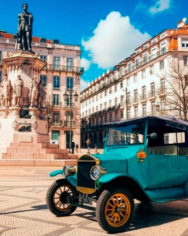 Carro antigo em uma praça com monumento e edifícios históricos ao fundo, céu azul claro com nuvens.