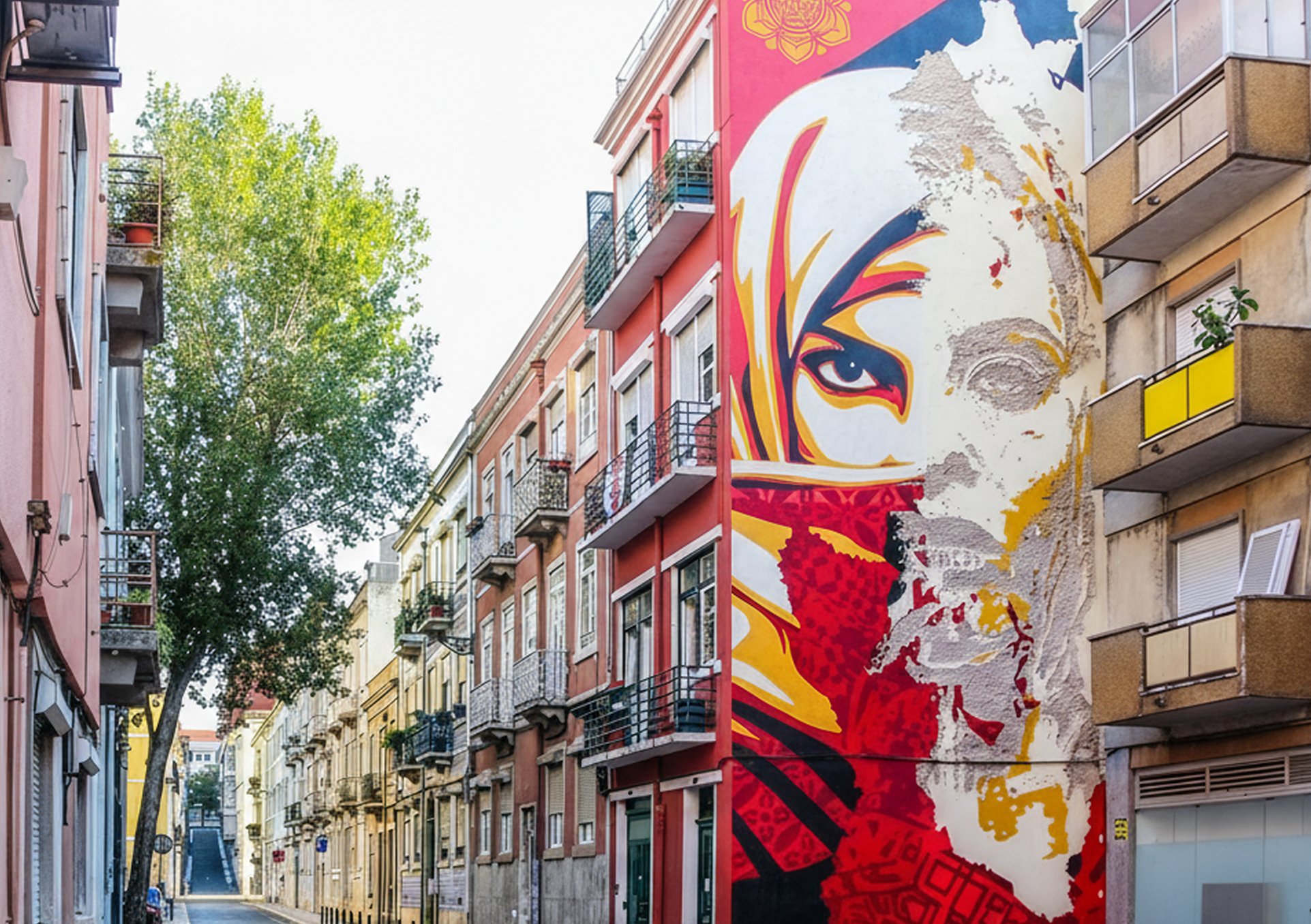 Rua com prédios residenciais coloridos e uma grande obra de arte mural de uma mulher com rosto parcialmente revelado na parede de um edifício.