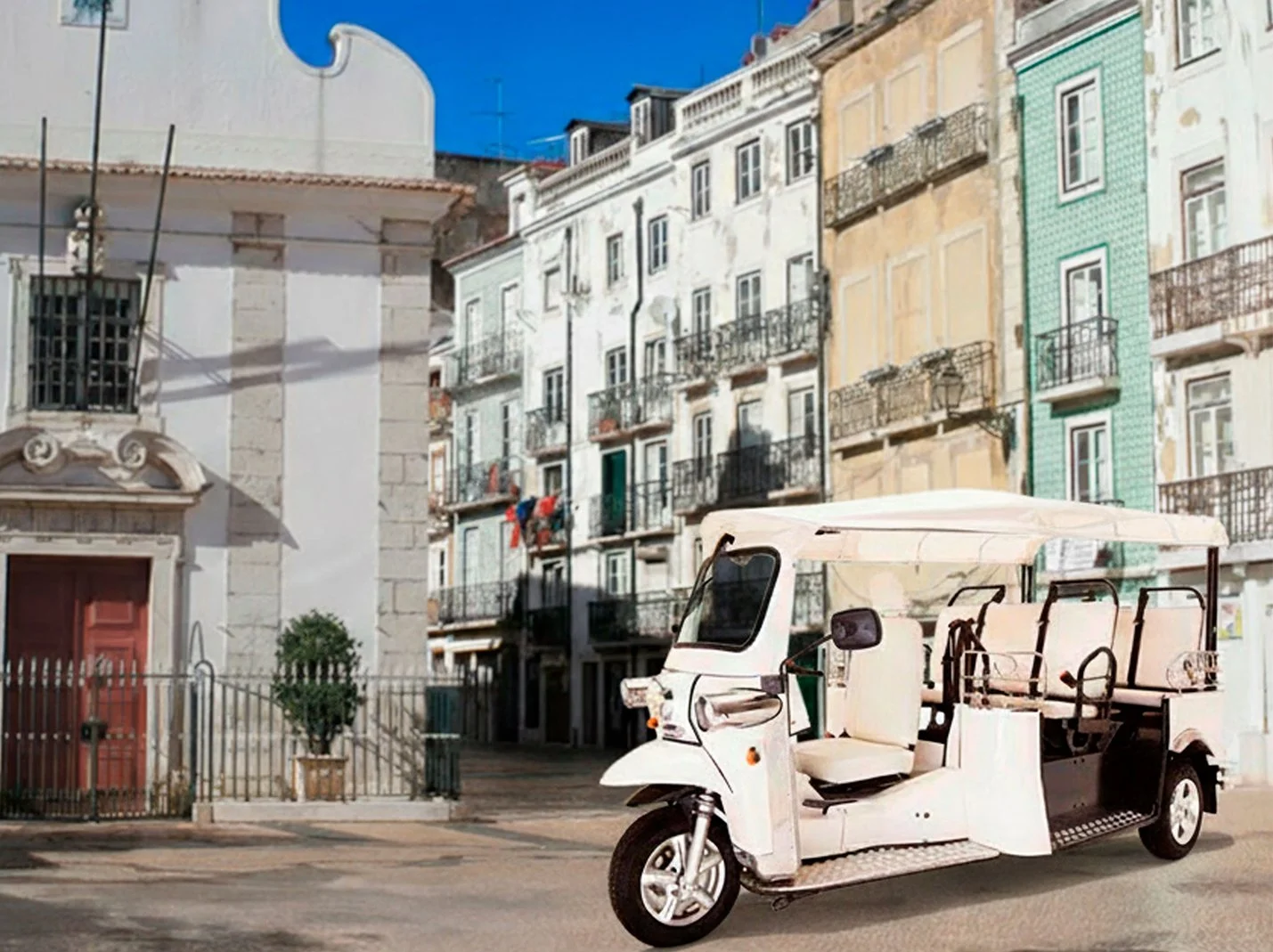 Uma rua com prédios antigos de apartamentos coloridos ao fundo e um carrinho de transporte de passageiros (tipo tuk-tuk) na frente, sob um céu azul.