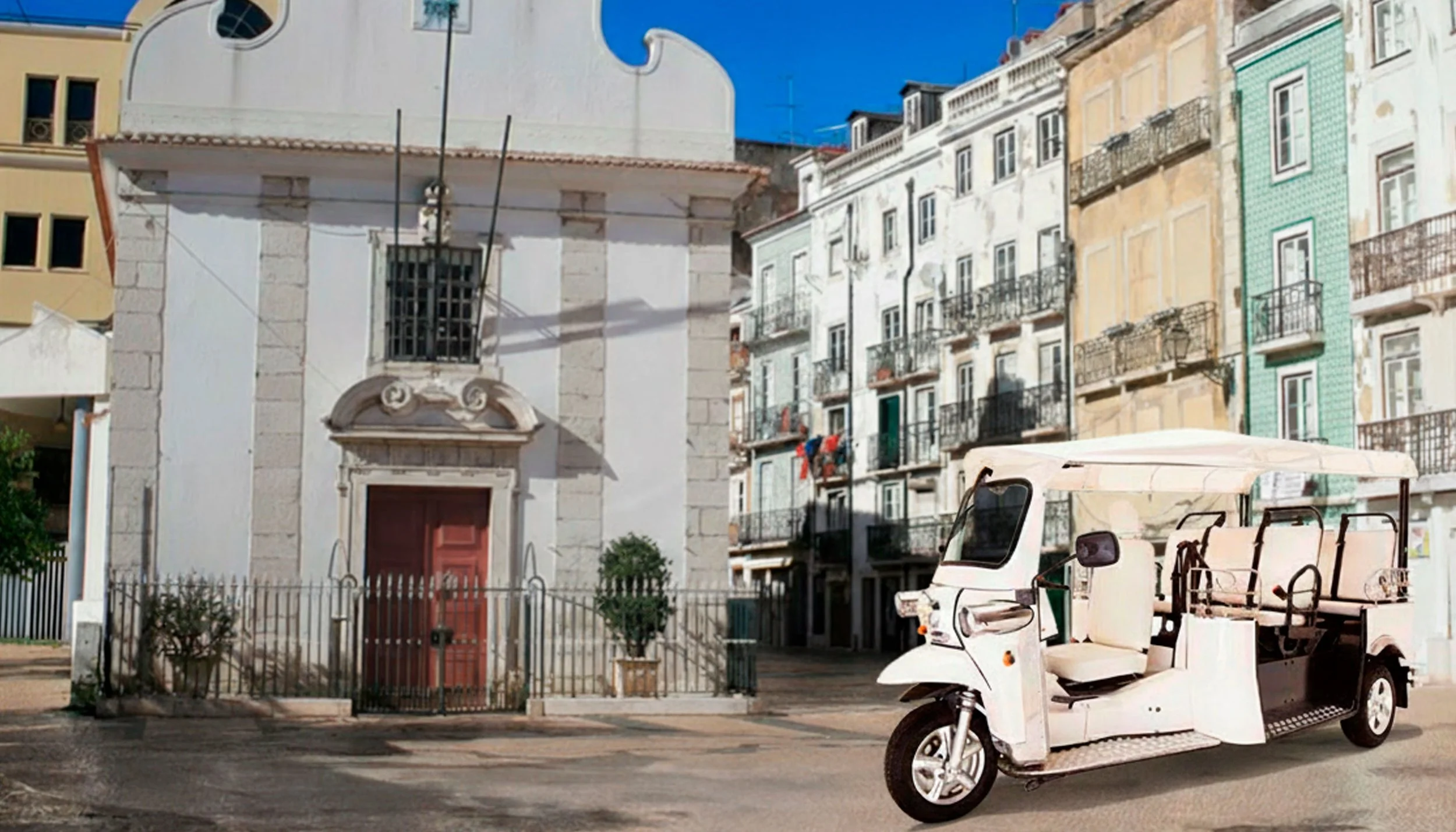 Táxi-poncho branco em frente a uma igreja antiga com fachada branca e detalhes em pedra, no centro de uma praça com edifícios coloridos ao fundo.