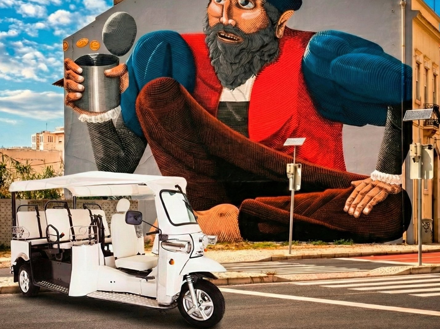 Mural de uma figura gigante de um homem com barba, usando roupas coloridas. Estacionado à frente, um triciclo elétrico de cor branca.