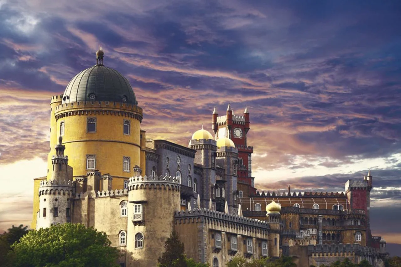 Castelo com torres, muralhas e cúpulas sob céu com nuvens coloridas ao pôr do sol.
