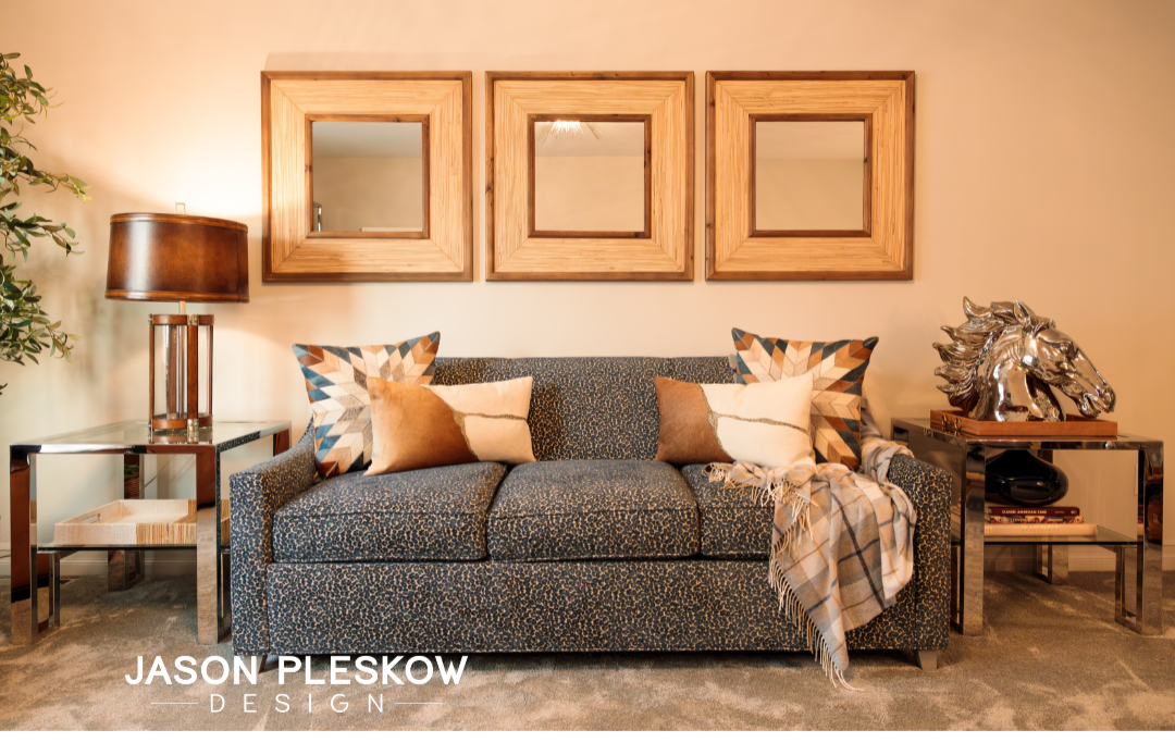 Living room with patterned sofa adorned with decorative pillows, framed mirrors above, side tables with decor, and a nearby plant.