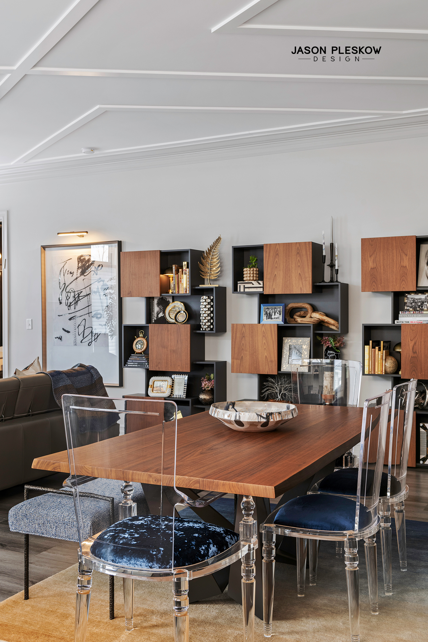 Modern dining room with wooden table, clear acrylic chairs, and black accent wall with wooden shelving units displaying decor and books.