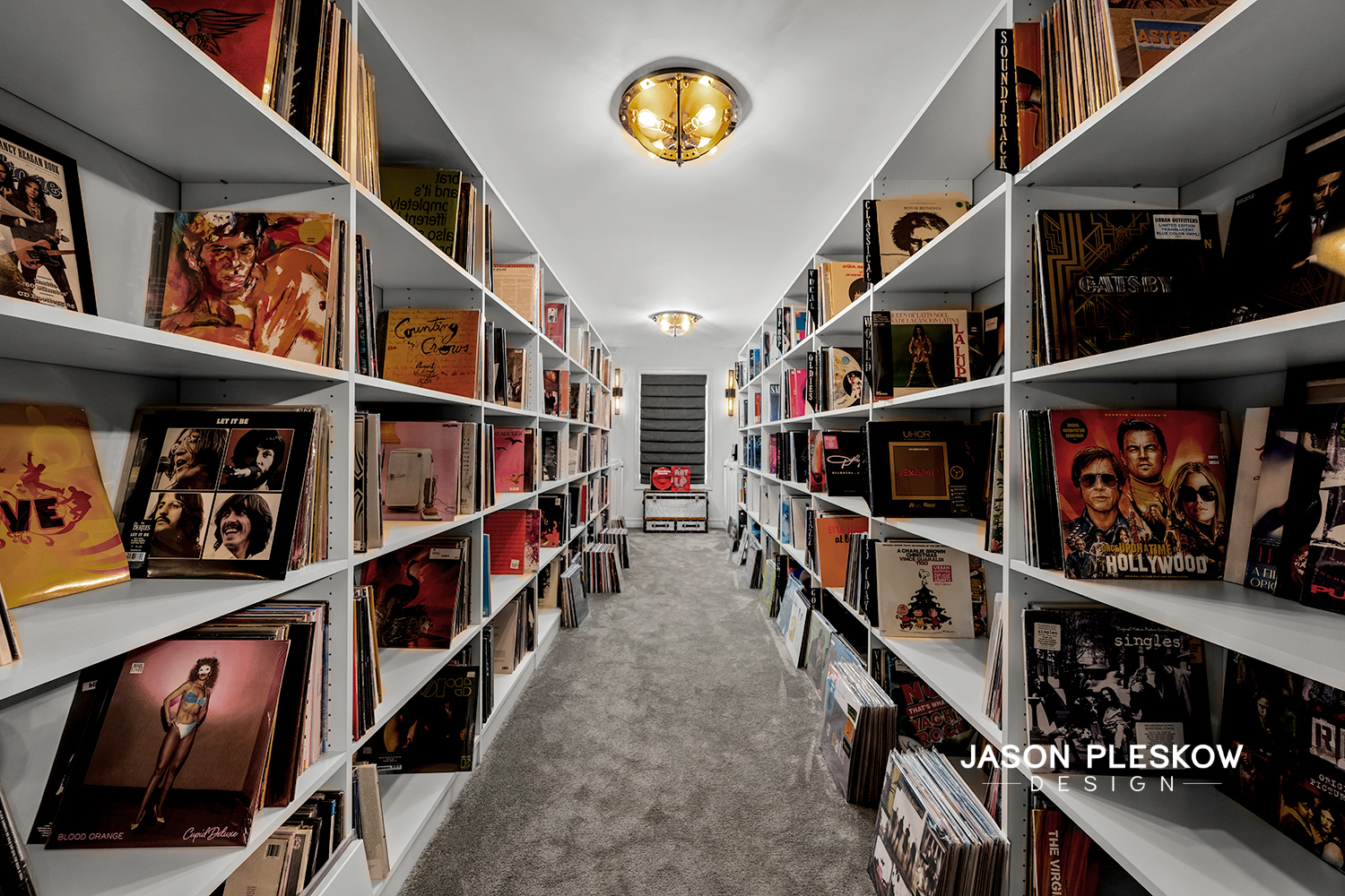 Inside a bookstore with white shelves filled with vinyl records on both sides of a narrow aisle, and a window at the back of the room.