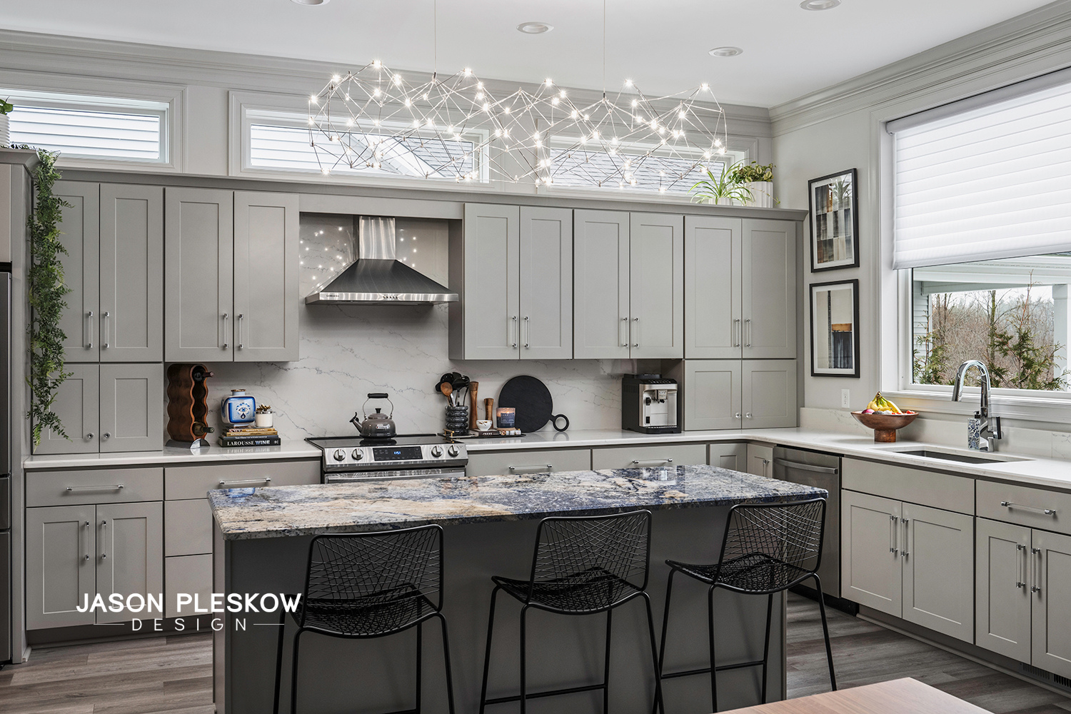 Modern kitchen with gray cabinets, marble backsplash, granite island, black wire chairs, and large window with white blinds.