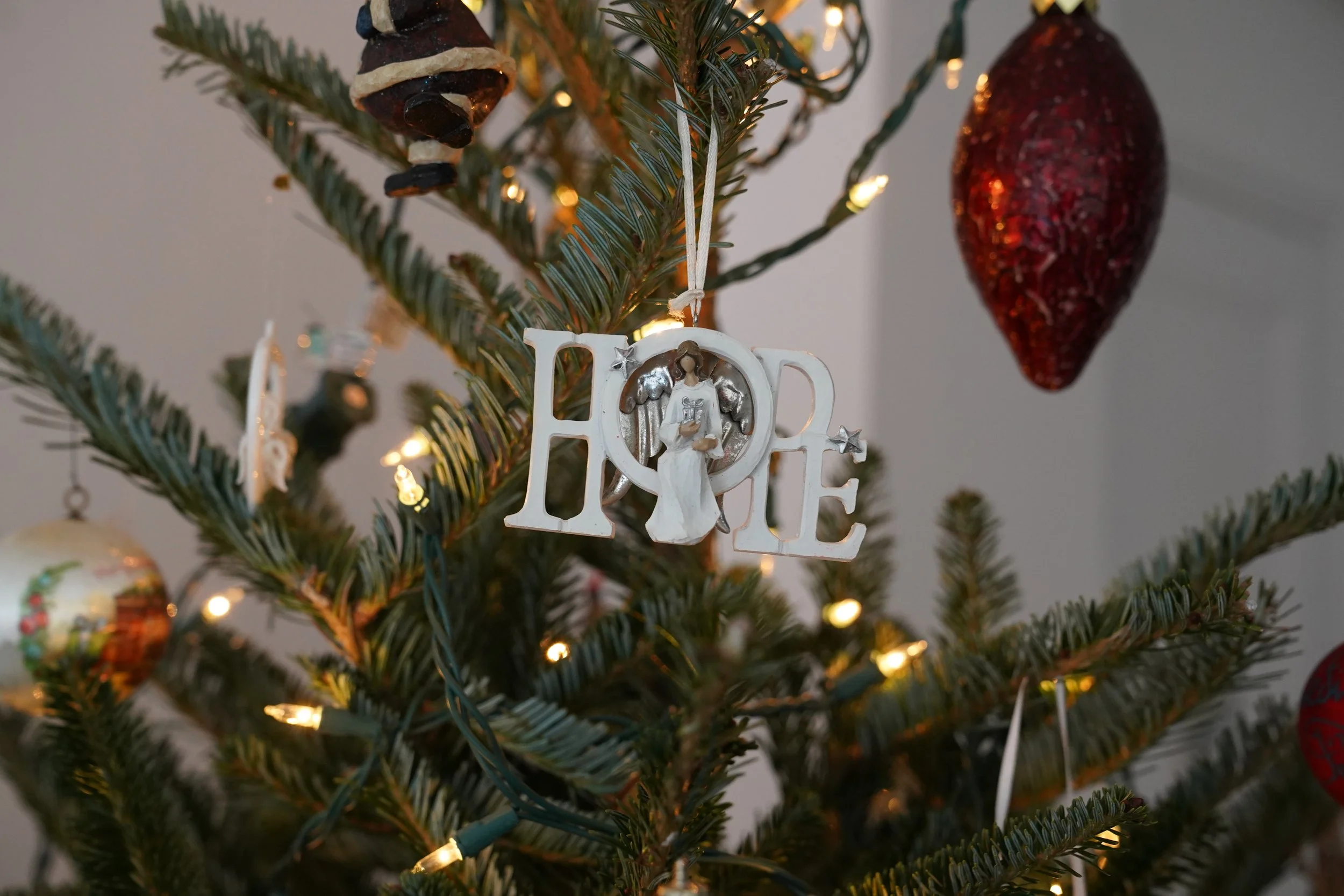Close-up of a decorated Christmas tree with a white 'LOVE' ornament featuring a figure of an angel, surrounded by warm white lights and other ornaments.