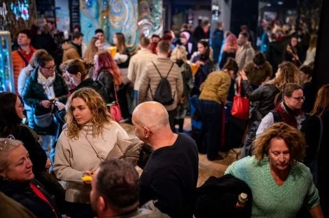 Crowd of people at an indoor event or gathering, many engaging in conversations and walking around.