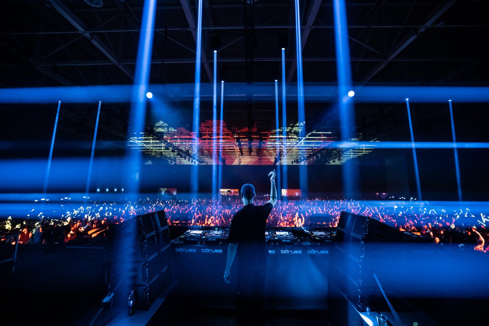 DJ performing at a concert with a large crowd and colorful light beams.