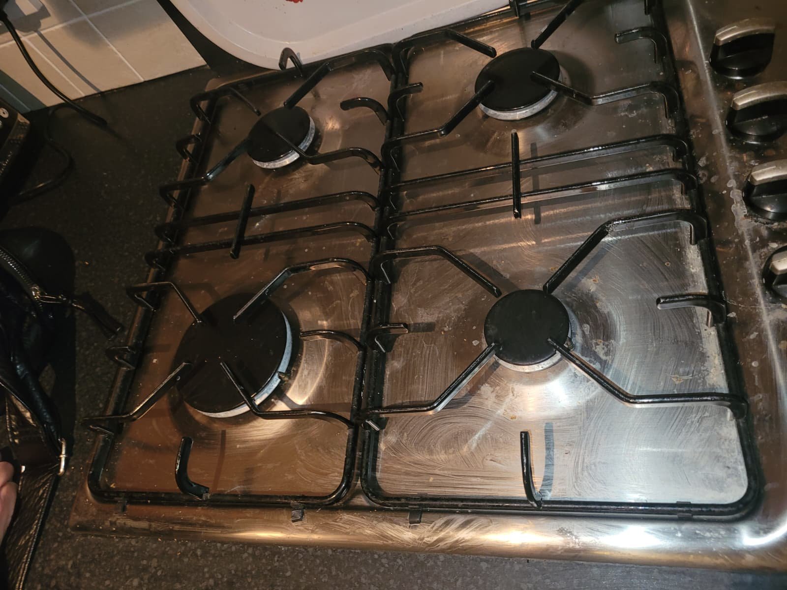 Stainless steel gas stove with four burners, black metal grates, and control knobs on the right side, with some smudges and stains visible on the surface.