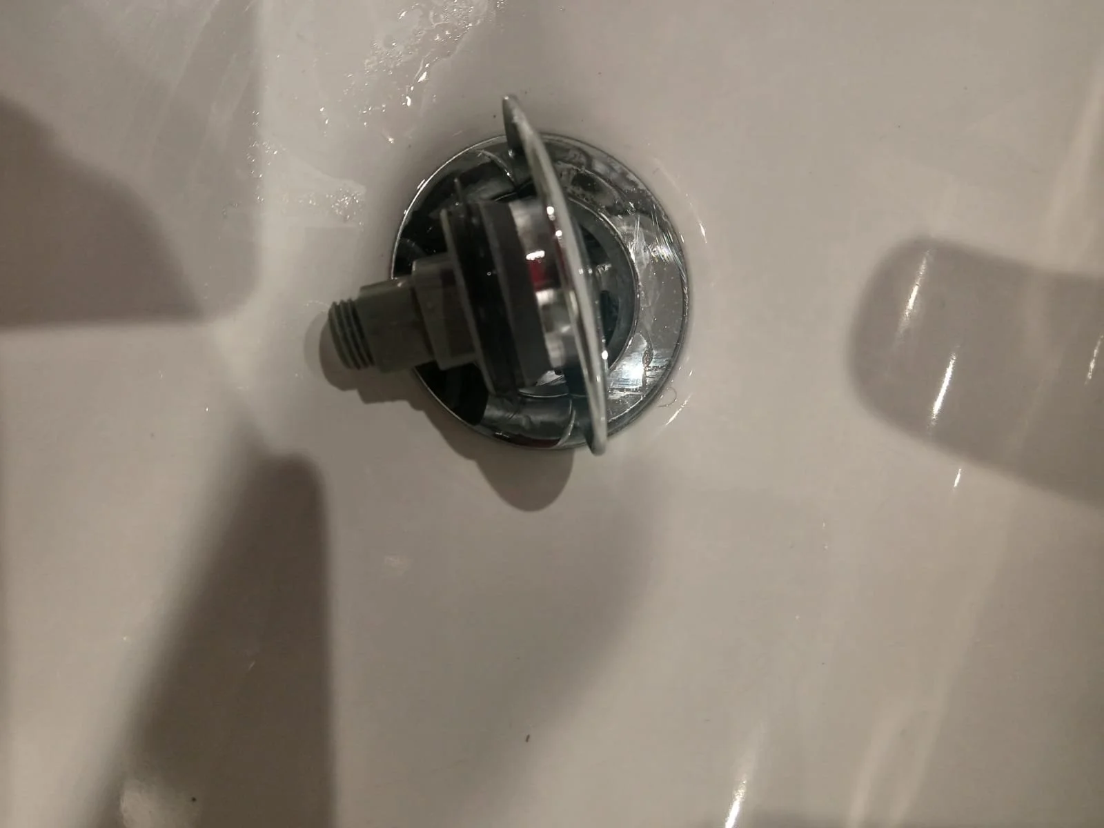 A close-up view of a sink drain with a detached drain component including a screw, inside a bathroom sink.