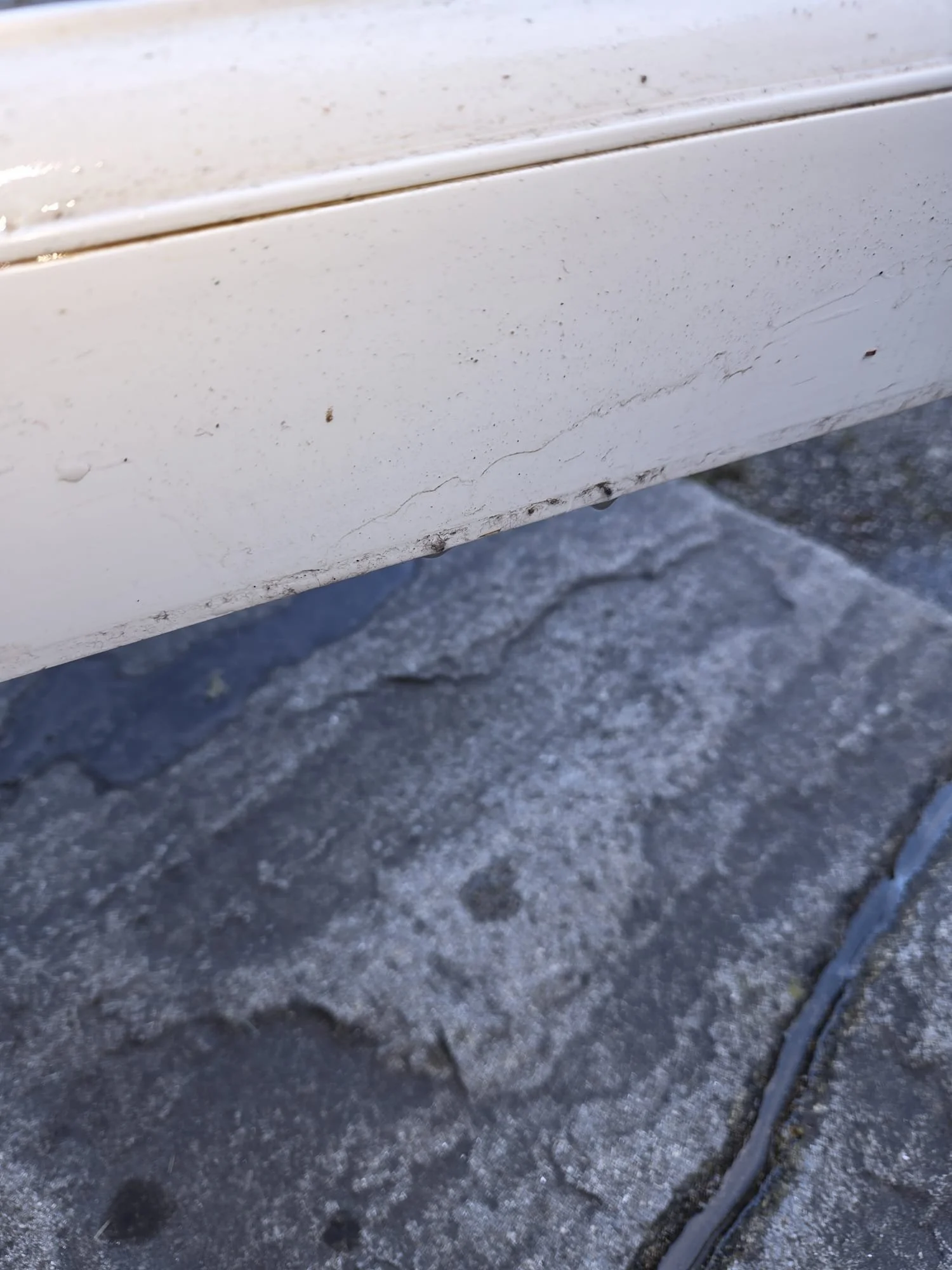 Close-up of a white painted surface with visible cracks and dirt, next to a textured gray stone pavement.