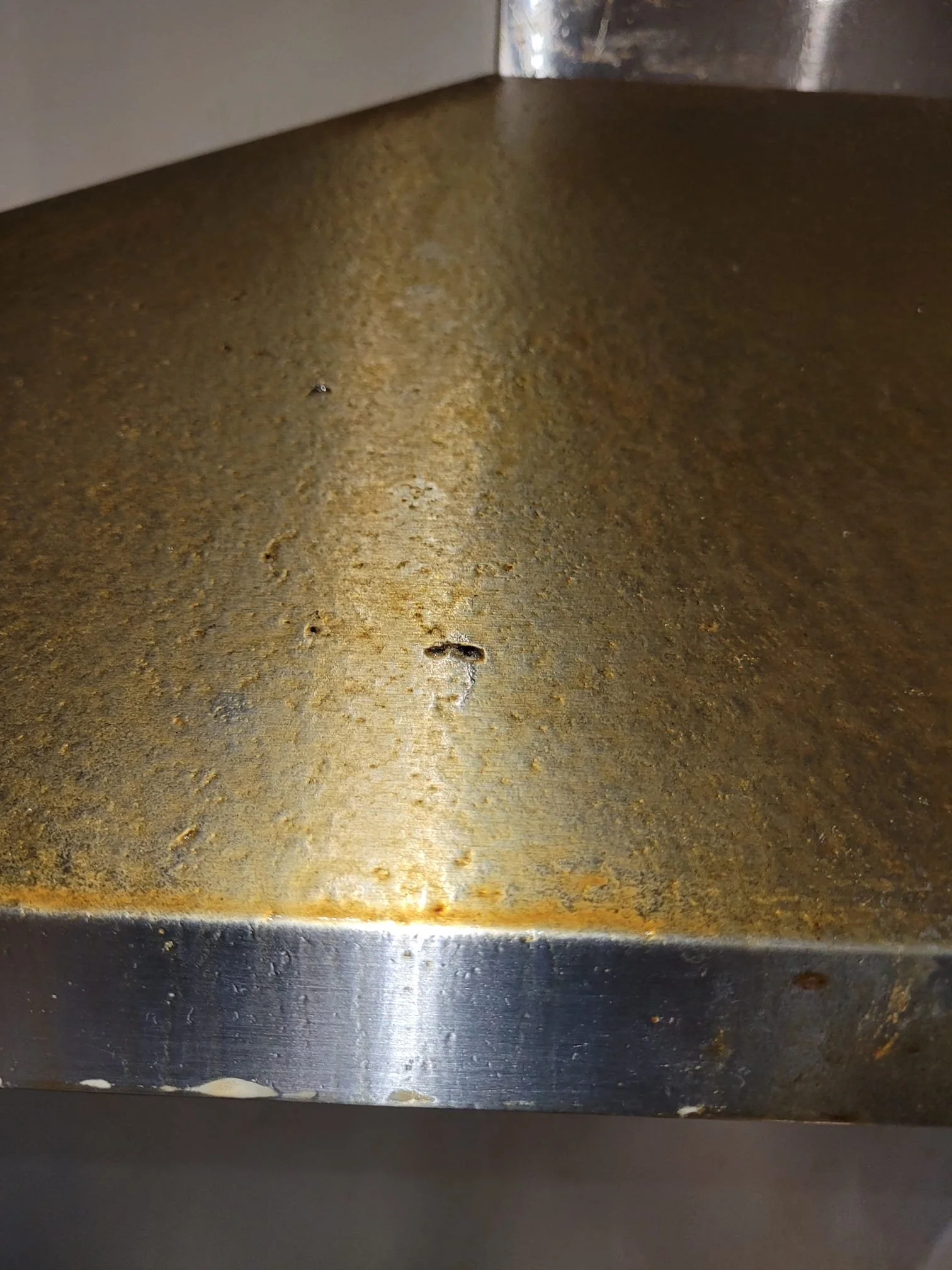 Close-up photo of a rusty, metallic kitchen range hood with visible rust spots and dents.