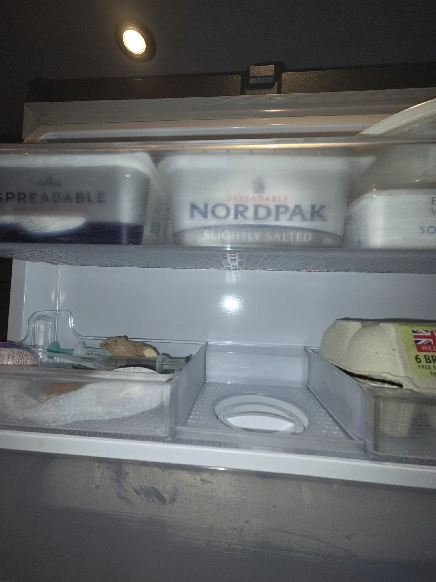 Inside a refrigerator with containers of spreadable butter on the top shelf and eggs on the lower shelf.