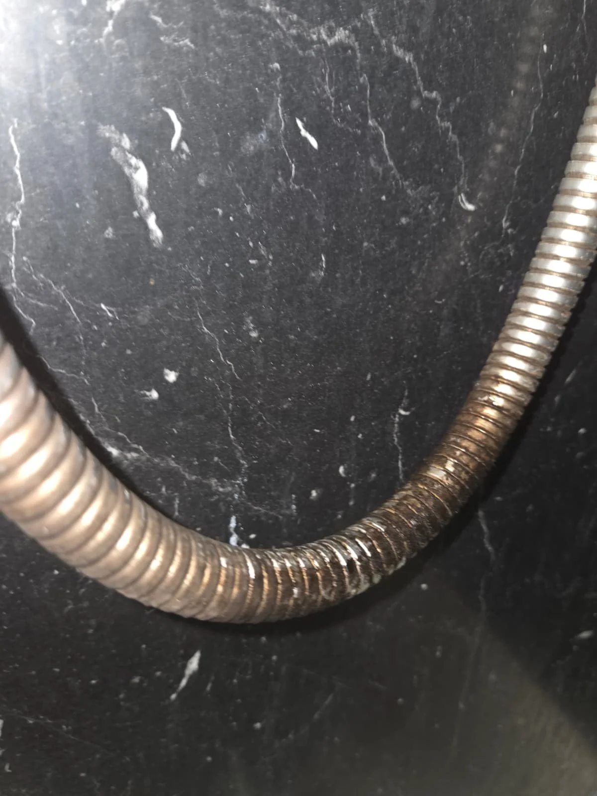 Close-up of a metal coiled hose against a black marble surface.