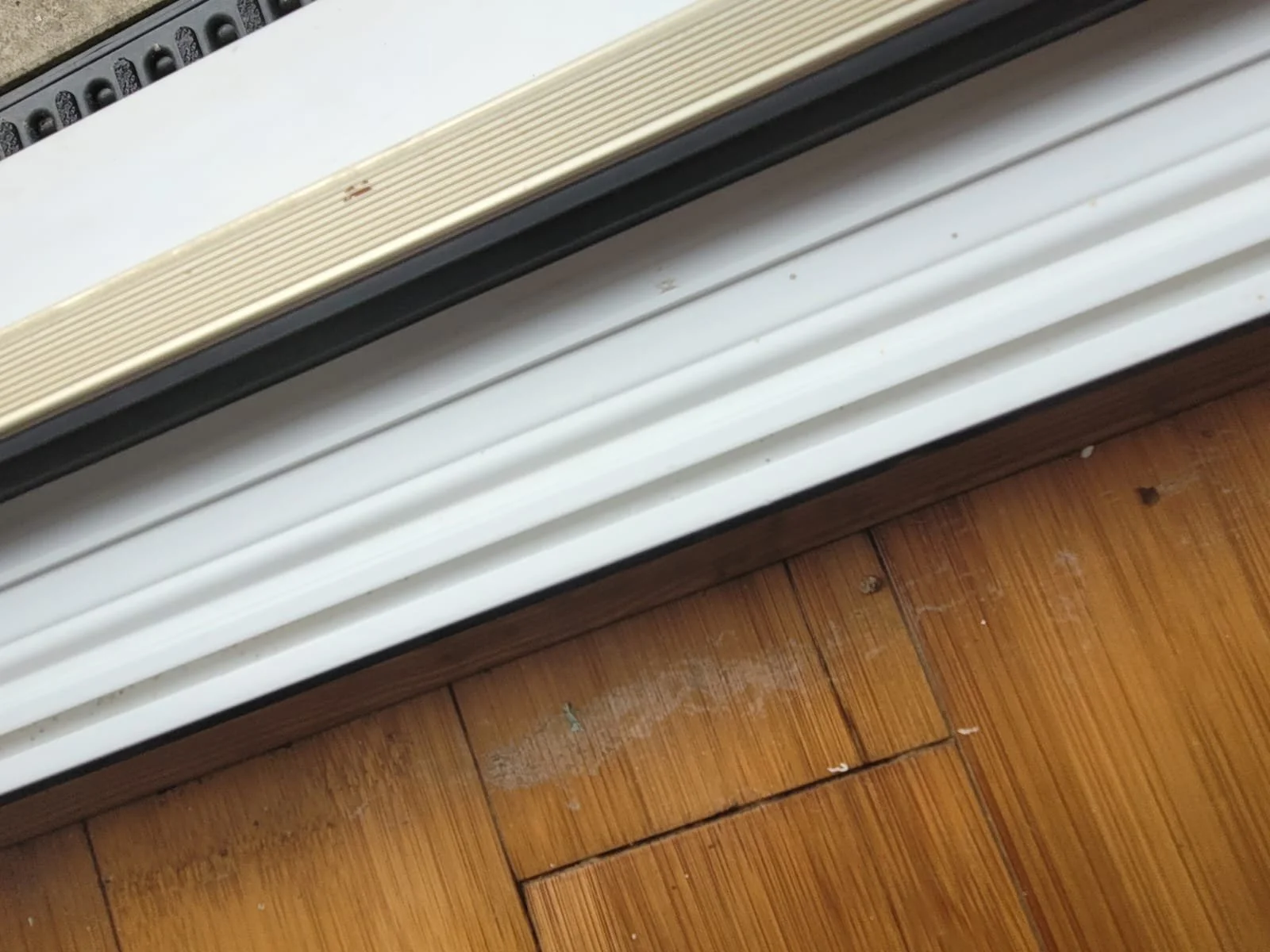 Close-up of a white metallic window or door shutter resting against a hardwood floor.