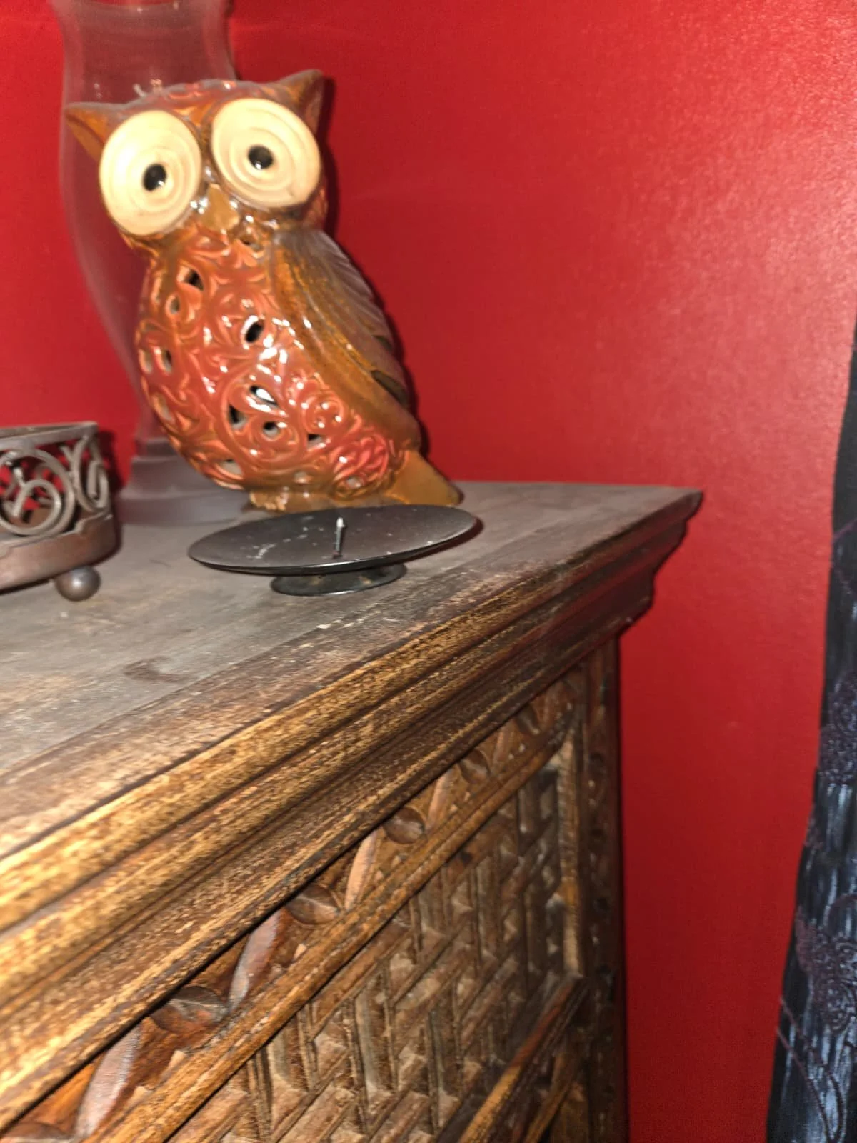 Decorative owl figurine on a wooden surface, against a red wall, with a black candle holder nearby.