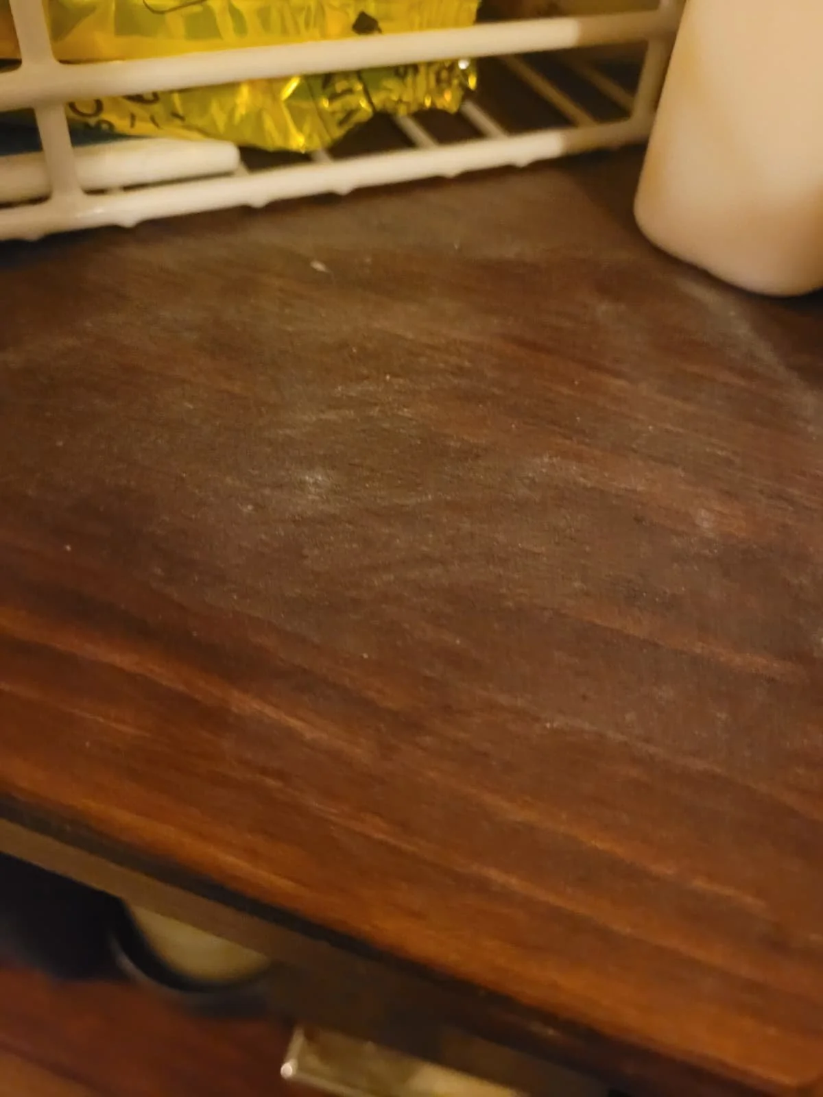 Close-up of a wooden surface with a white wire shelf and some objects on top.