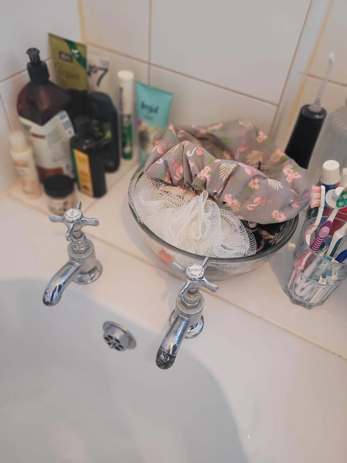 Bathroom sink with various toiletries on the countertop, including soap, lotion, toothbrushes, toothpaste, and a bowl with toiletries.