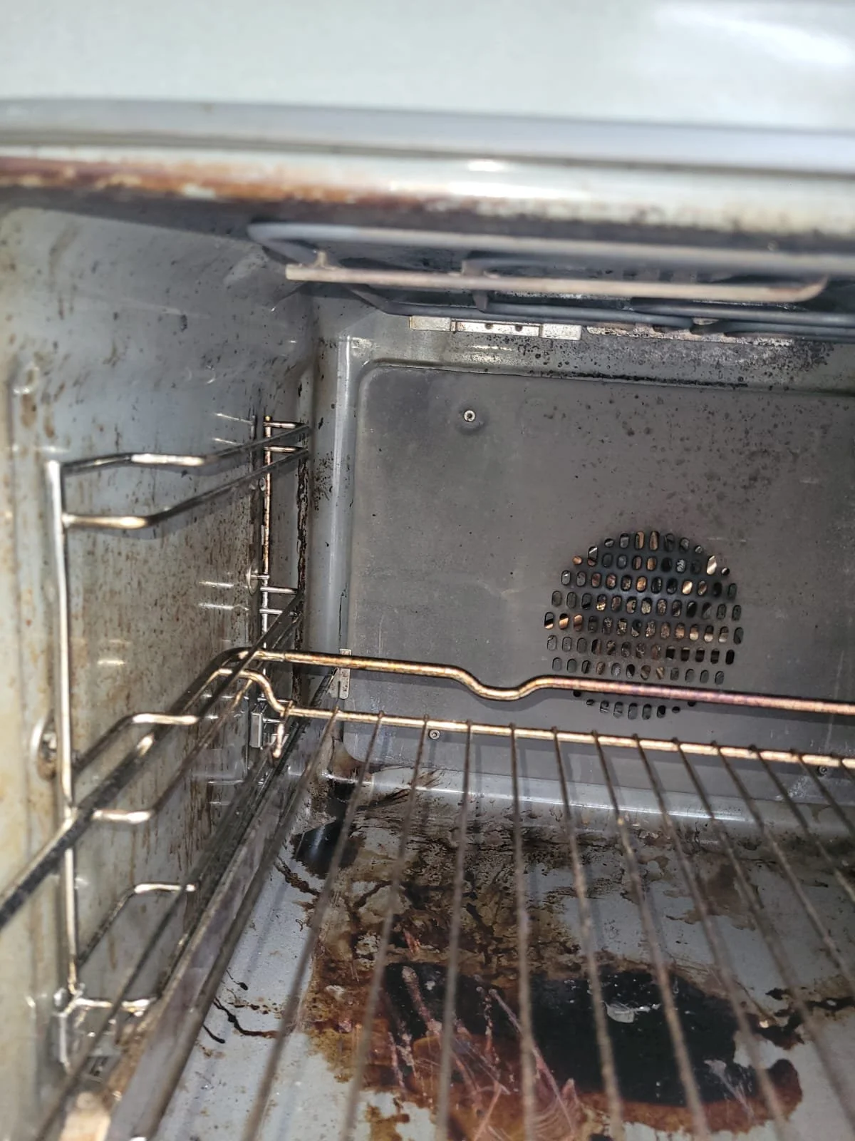 Inside a dirty and greasy oven with burnt food and stains on the bottom surface and walls.