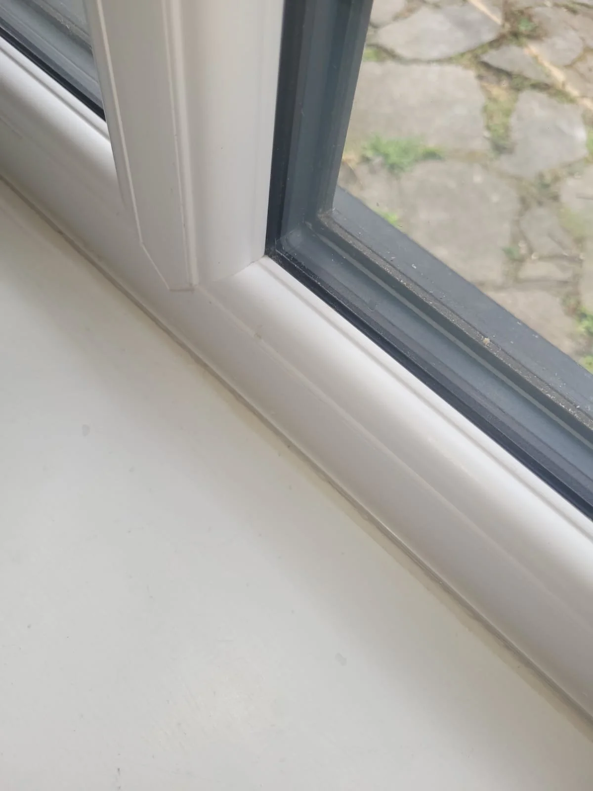 Close-up of a window frame and windowsill with a view of a stone patio outside.