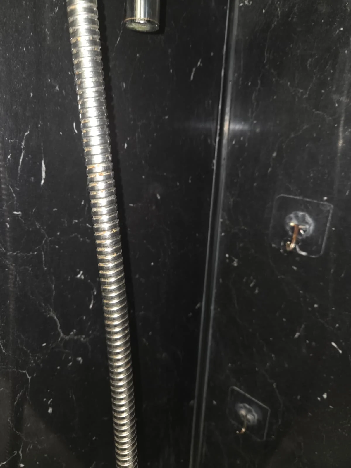 Close-up of a black surface with a metallic flexible hose and hardware screws.