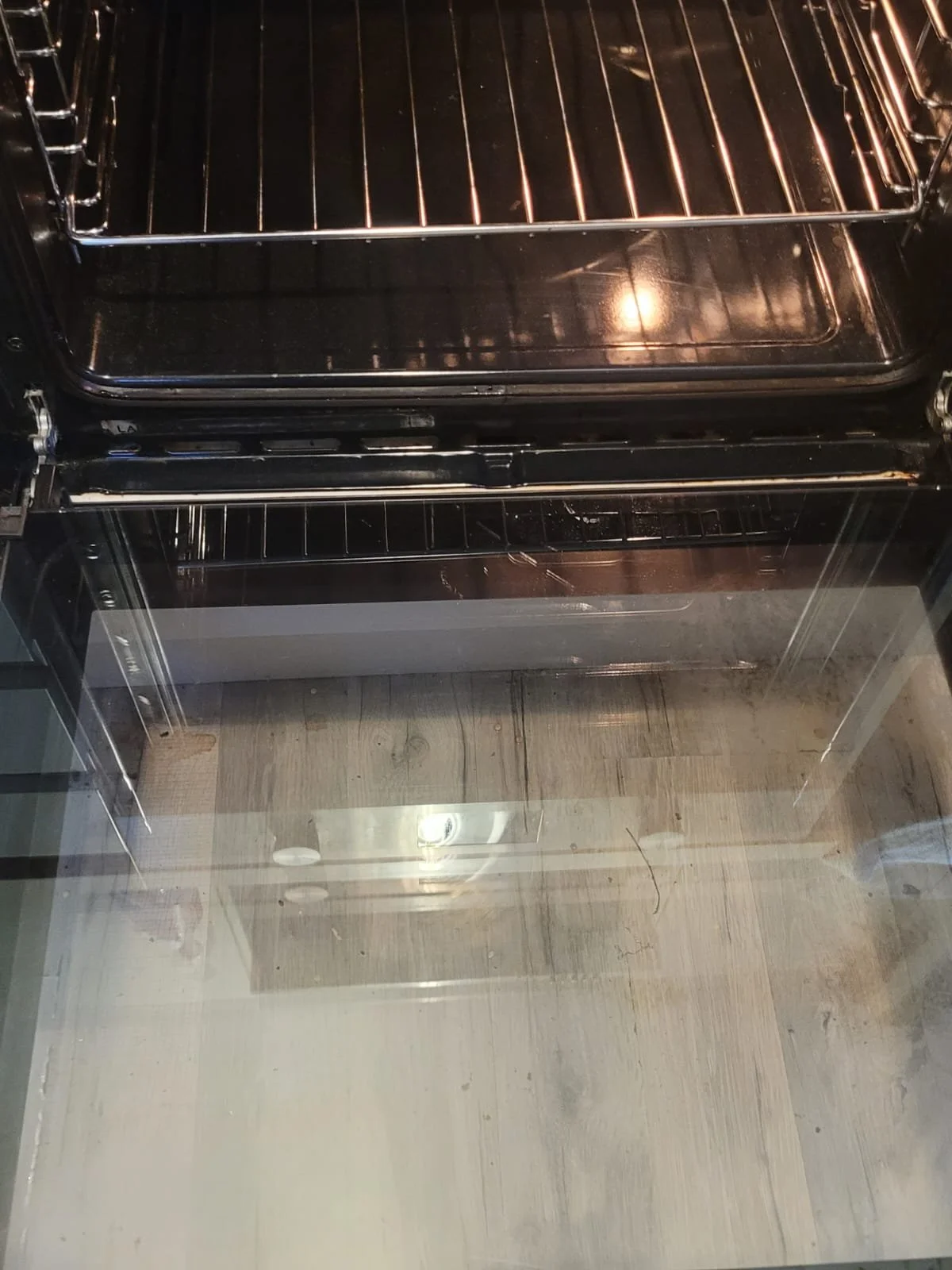 Inside of a clean oven with two racks, no food present, viewed from the open door showing the glass panel and the wooden floor in front.