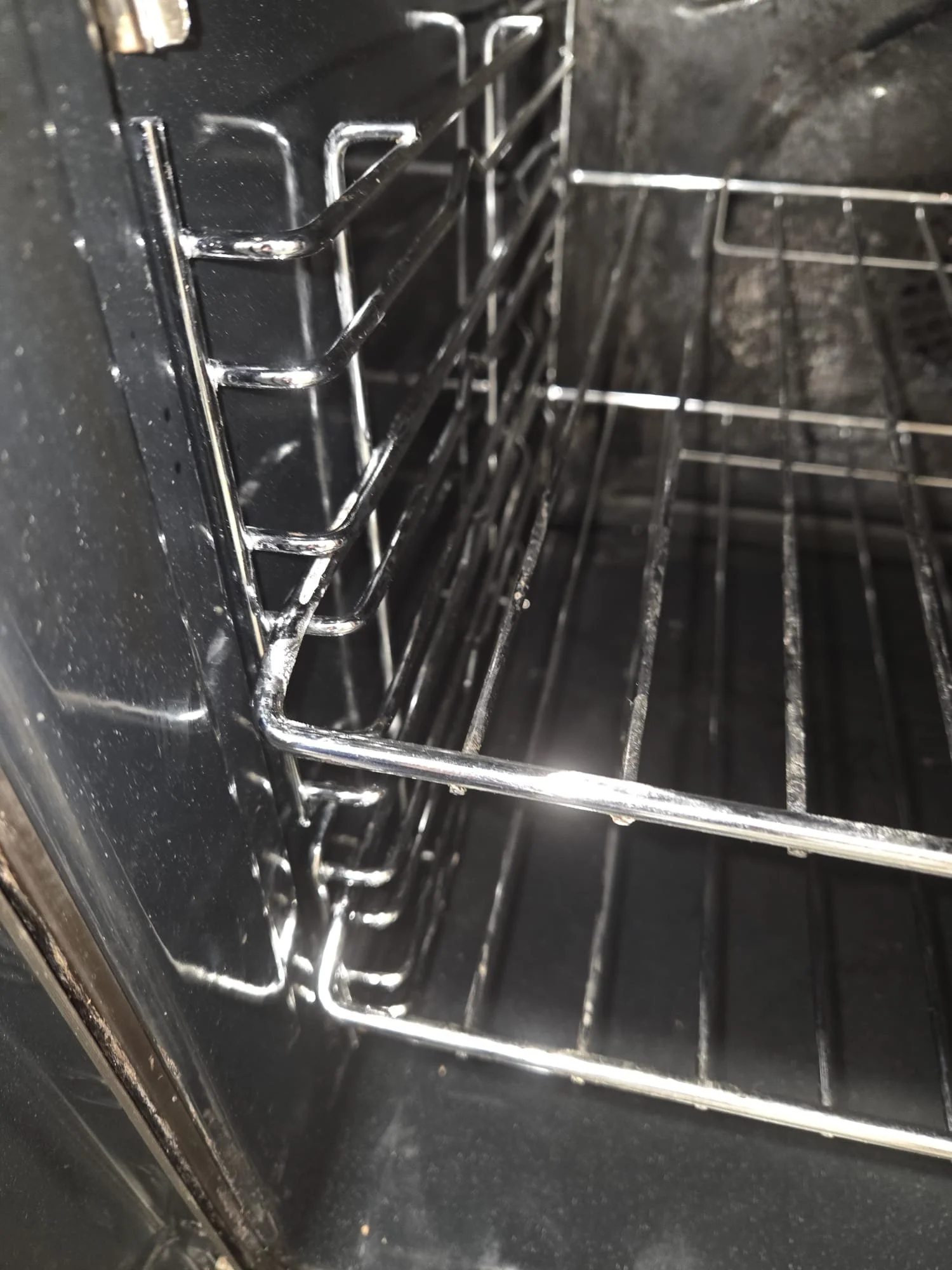 Inside of an empty black oven with metal racks installed.