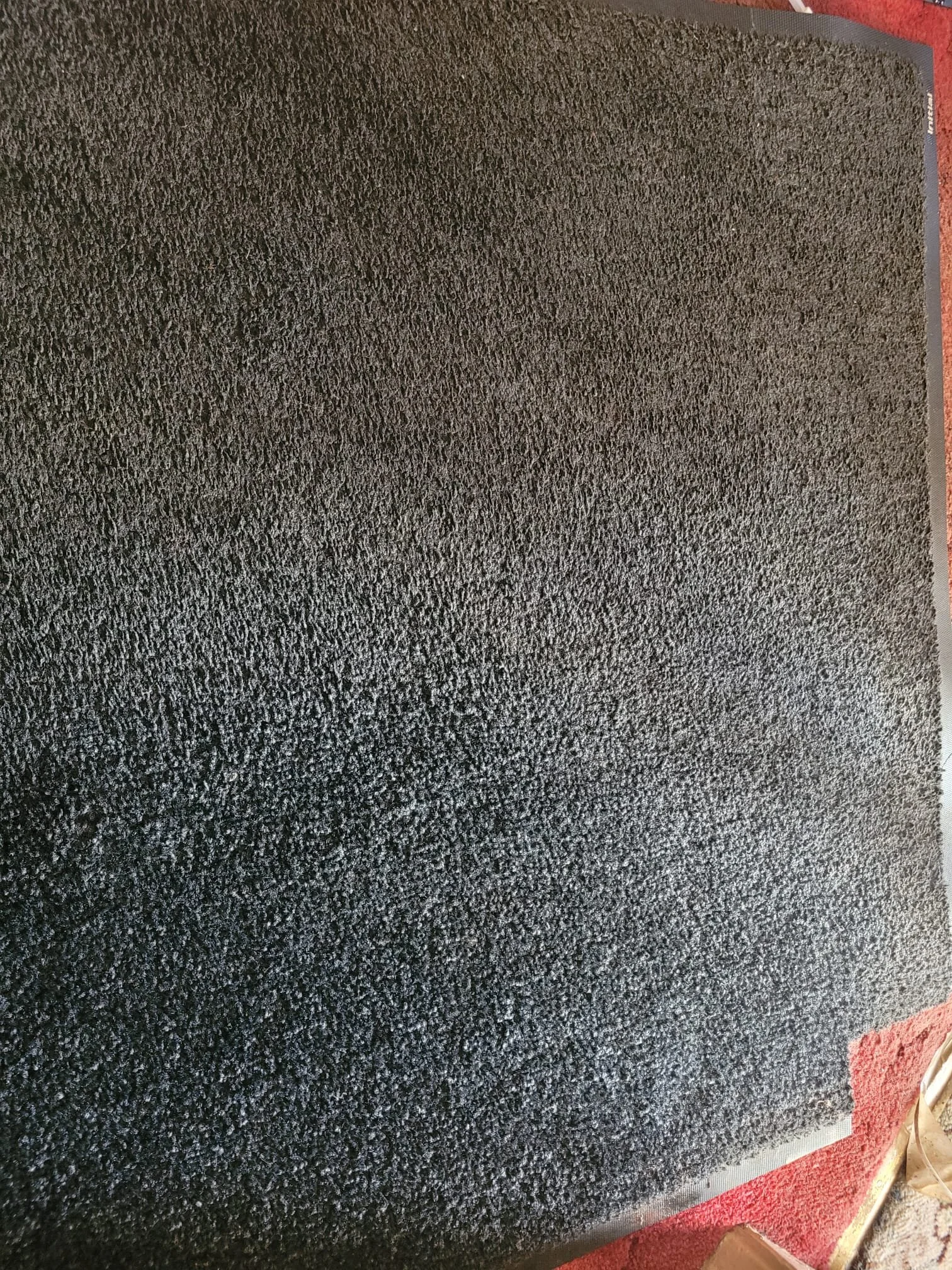 A close-up view of a black textured doormat or rug on a red surface.