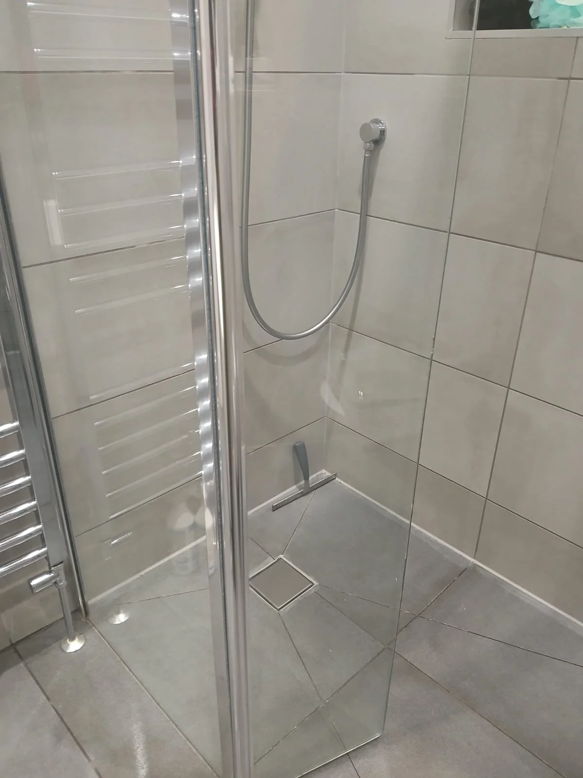 Empty shower stall with beige tiled walls, a handheld showerhead, and a glass door.