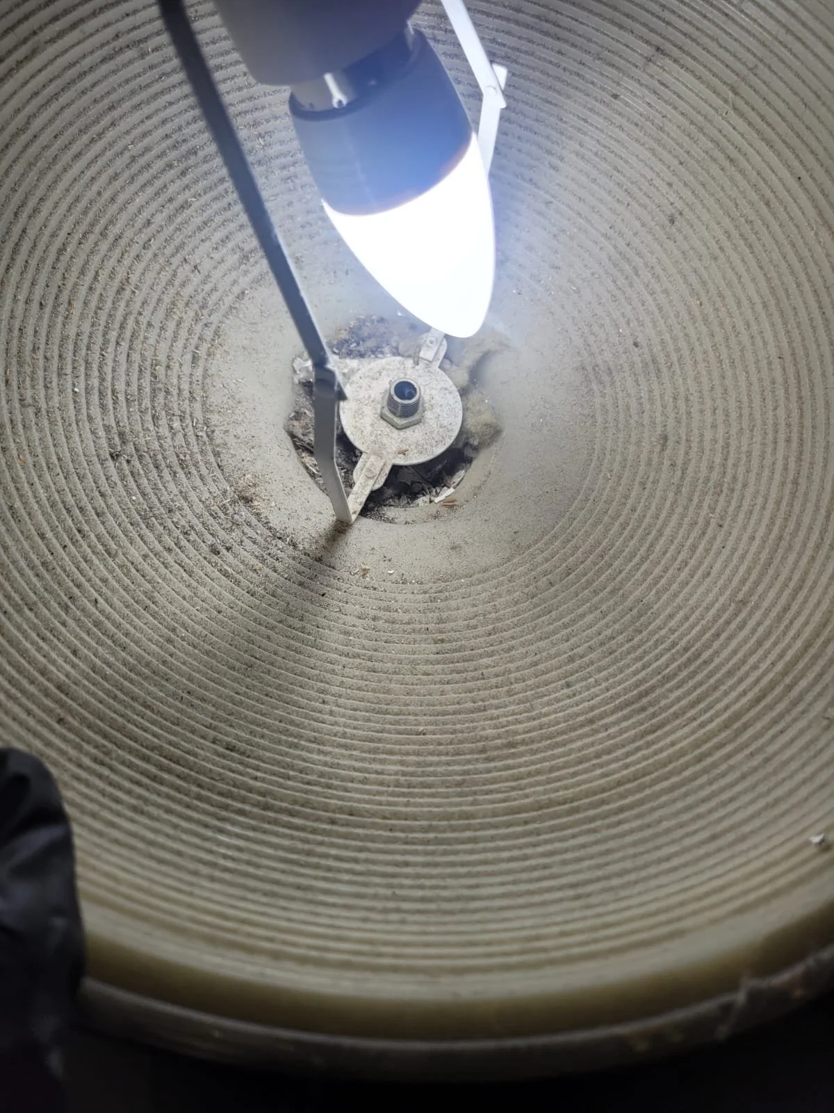 Close-up view inside a tall, cylindrical outdoor lamp post illuminated by a bright light bulb at the top.