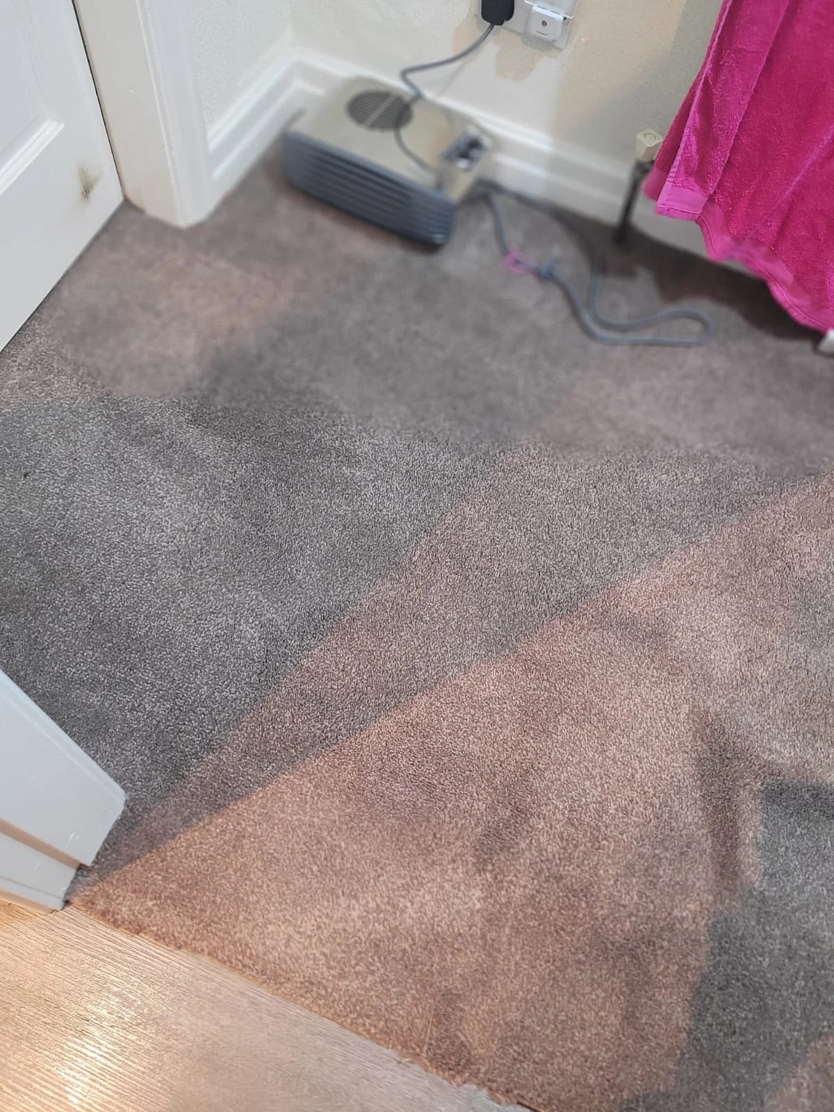 A room corner with a multicolored carpet and a pink towel hanging on the side. An electric heater is plugged into an outlet on the wall.