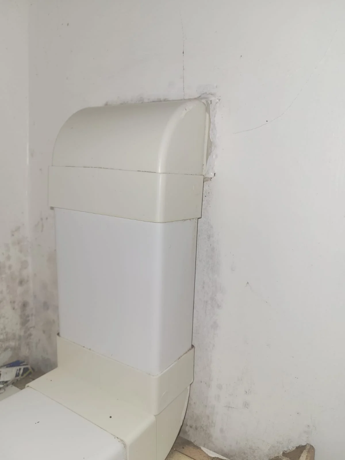 A white toilet with a closed lid, positioned against a wall with peeling paint and marks.