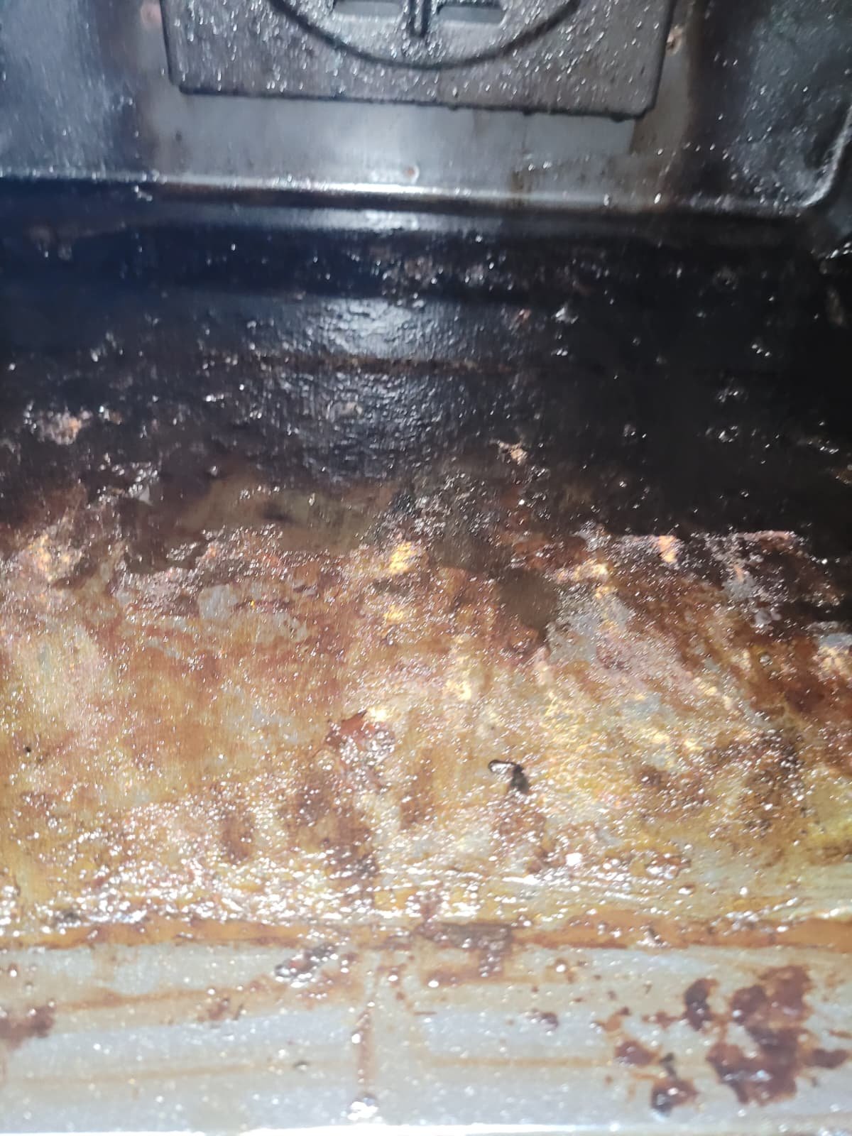 Grease and food residue inside a deep fryer or oven, with burnt bits and oil buildup.