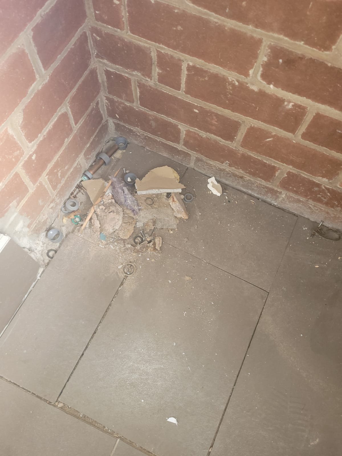 Construction area with debris, bricks, and plumbing fittings at the corner of a brick wall and tiled floor.