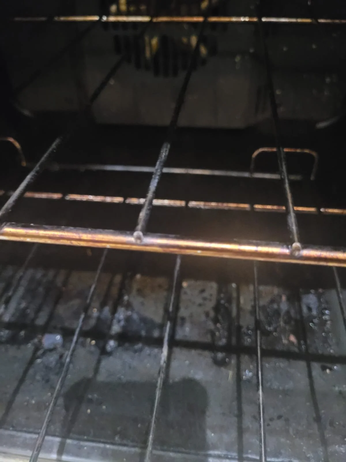 Inside of a dirty oven with dirty oven racks and burnt leftover debris at the bottom.